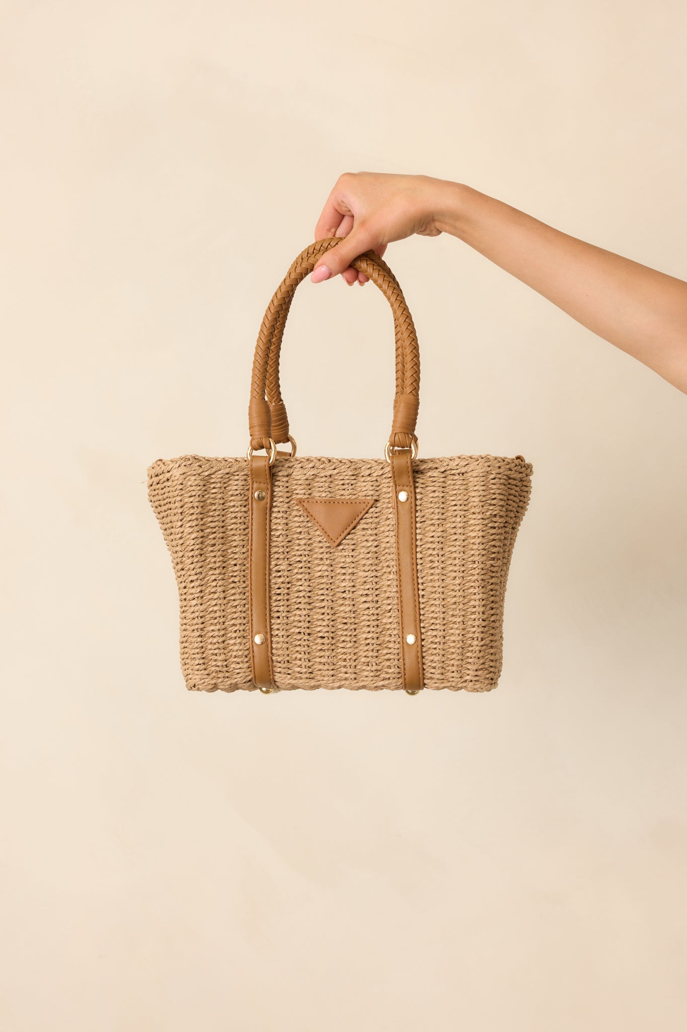 A handbag carried by brown faux leather handles, displaying the natural rattan texture and medium-sized rectangular shape.