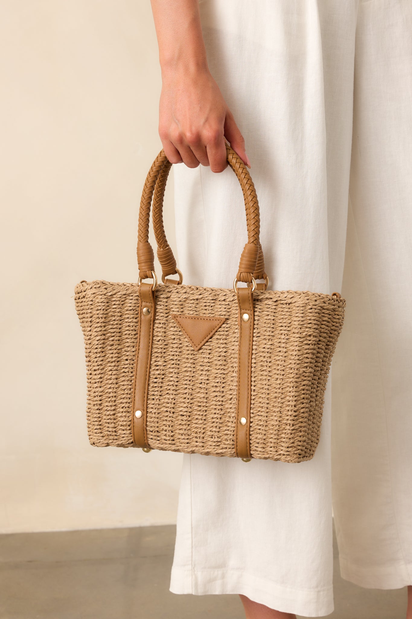 A front crop of the rattan handbag highlighting the woven material, faux leather details, and zippered top closure.