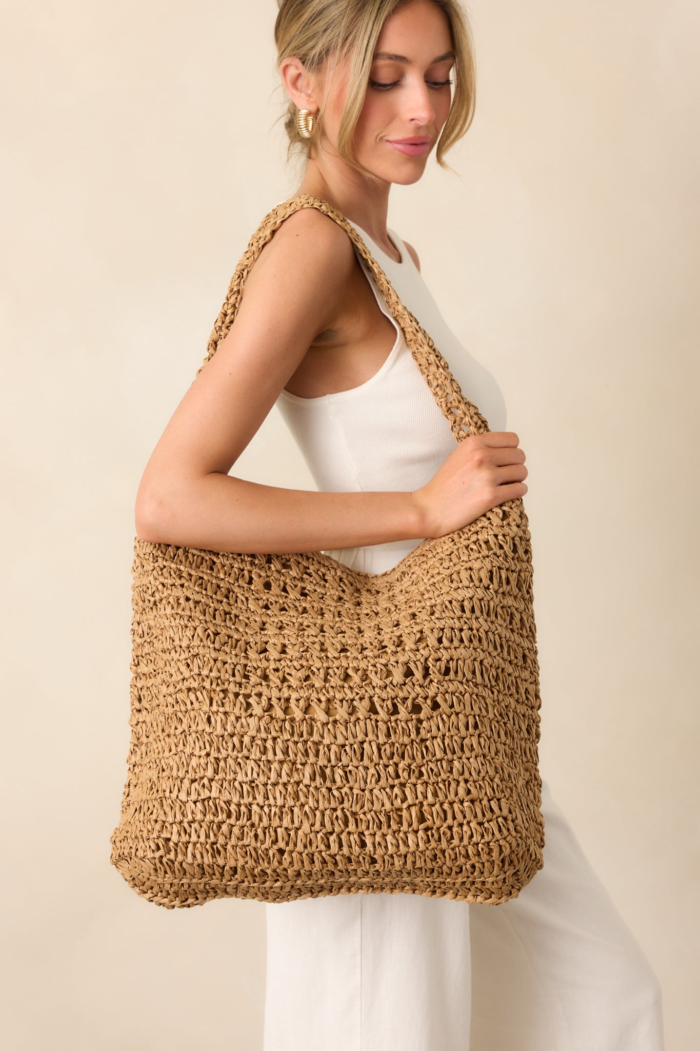 The tan raffia handbag with a wide single shoulder strap shown worn over the shoulder, highlighting its relaxed and roomy shape.