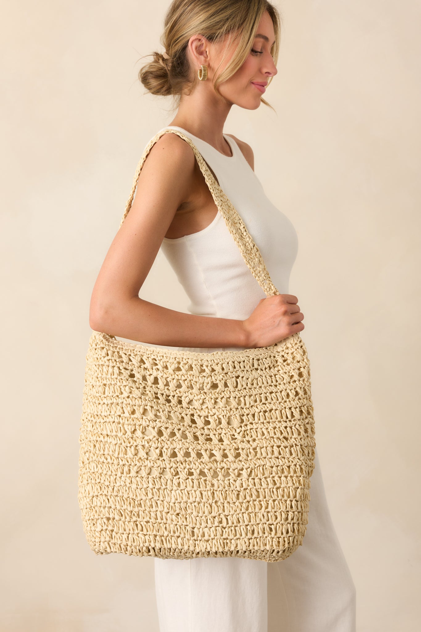 The ivory raffia handbag worn over the shoulder, showcasing its wide single strap and soft, slouchy silhouette.