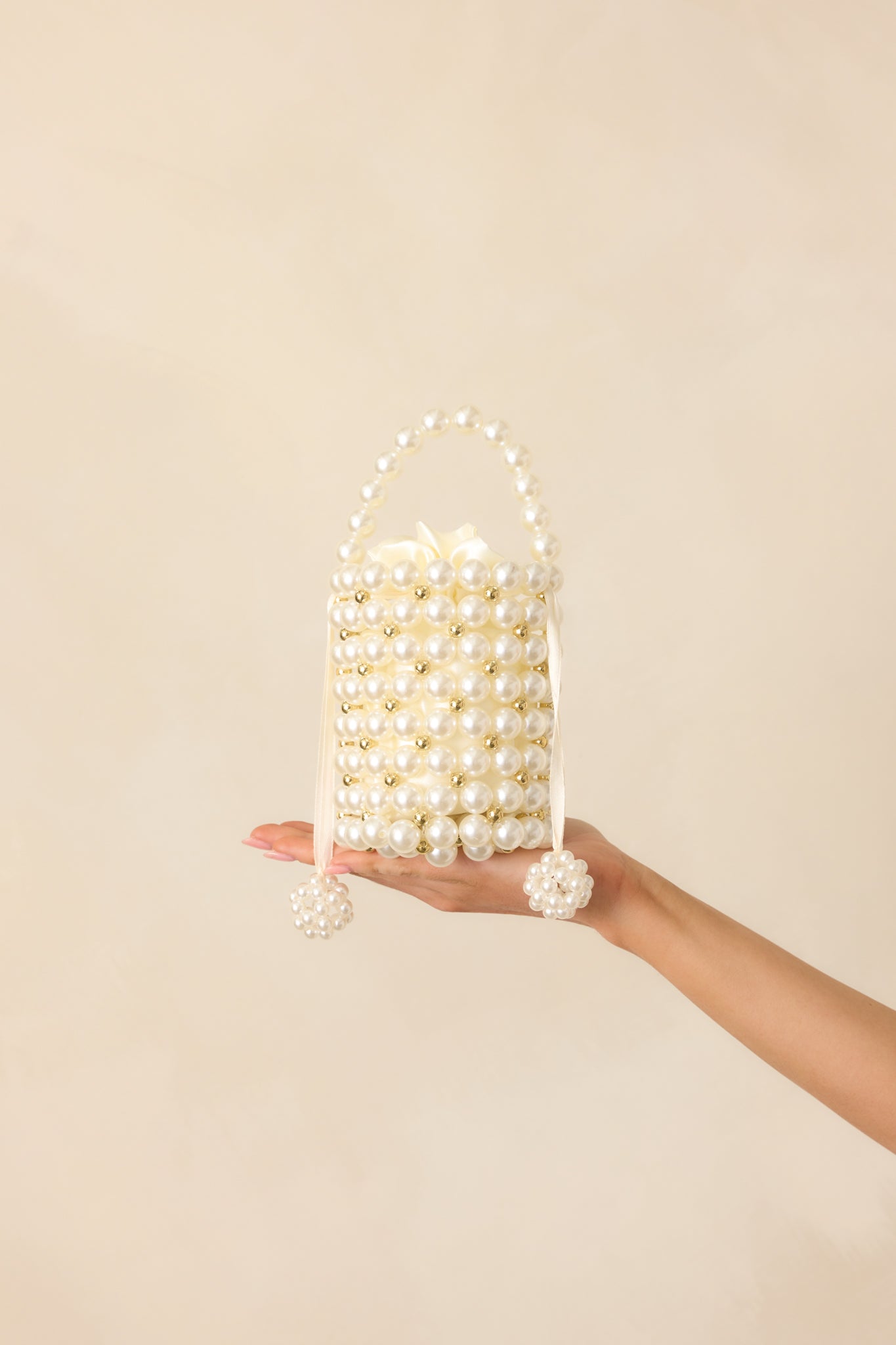 Full view of the cylindrical ivory pearl clutch showing the structured pearl handle, alternating gold and ivory pearls, and pearl charm tassels.