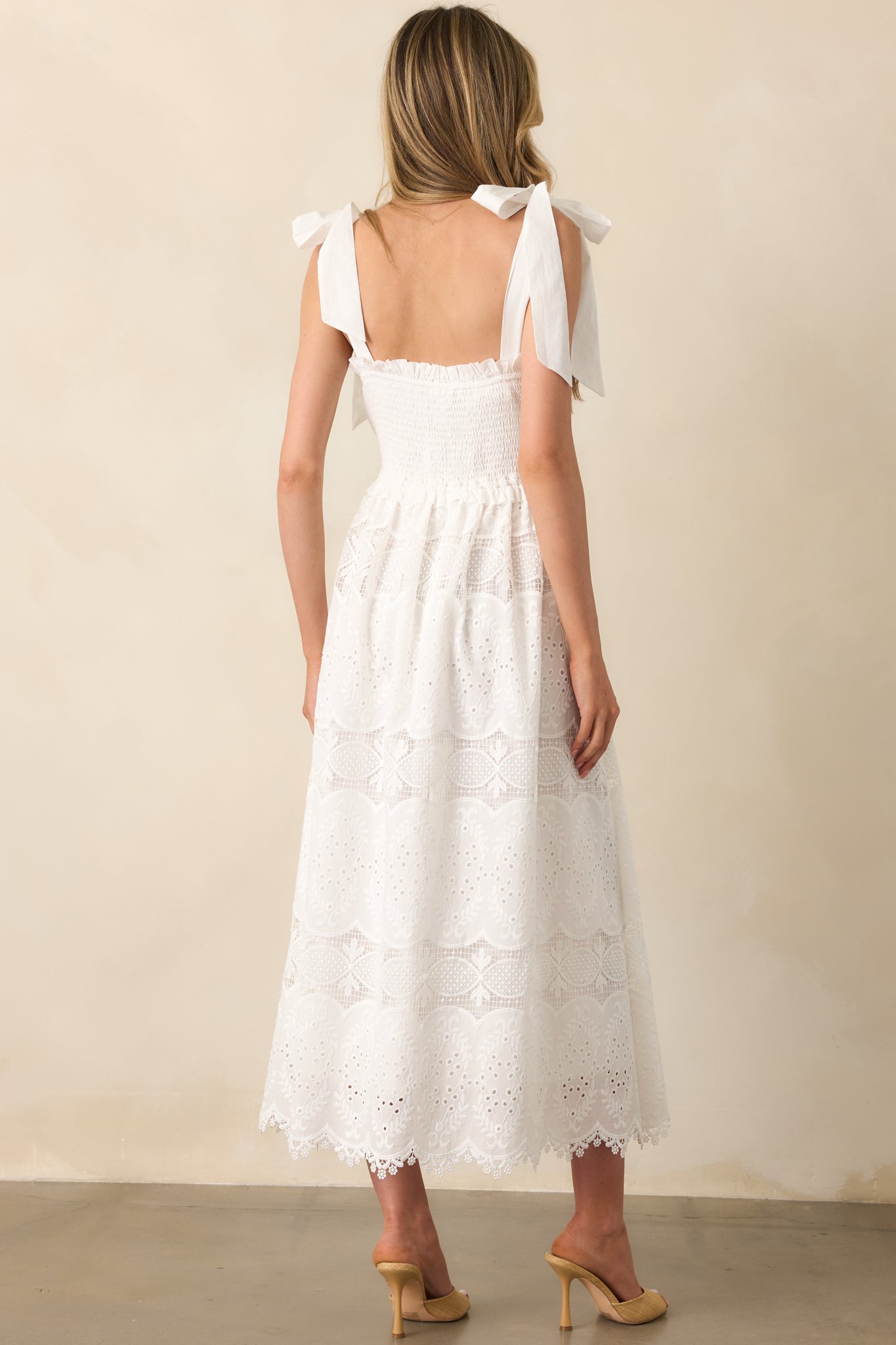 A view from behind of the white dress, displaying the smocked back, tie straps, and full embroidered overlay.