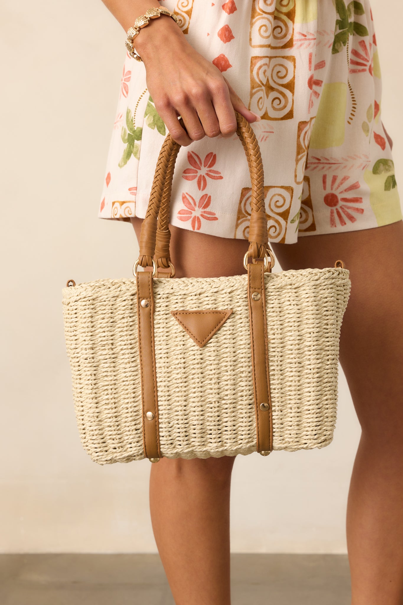 Full view of the ivory handbag with structured woven handles and tan faux leather accents, highlighting the rattan material and overall silhouette.