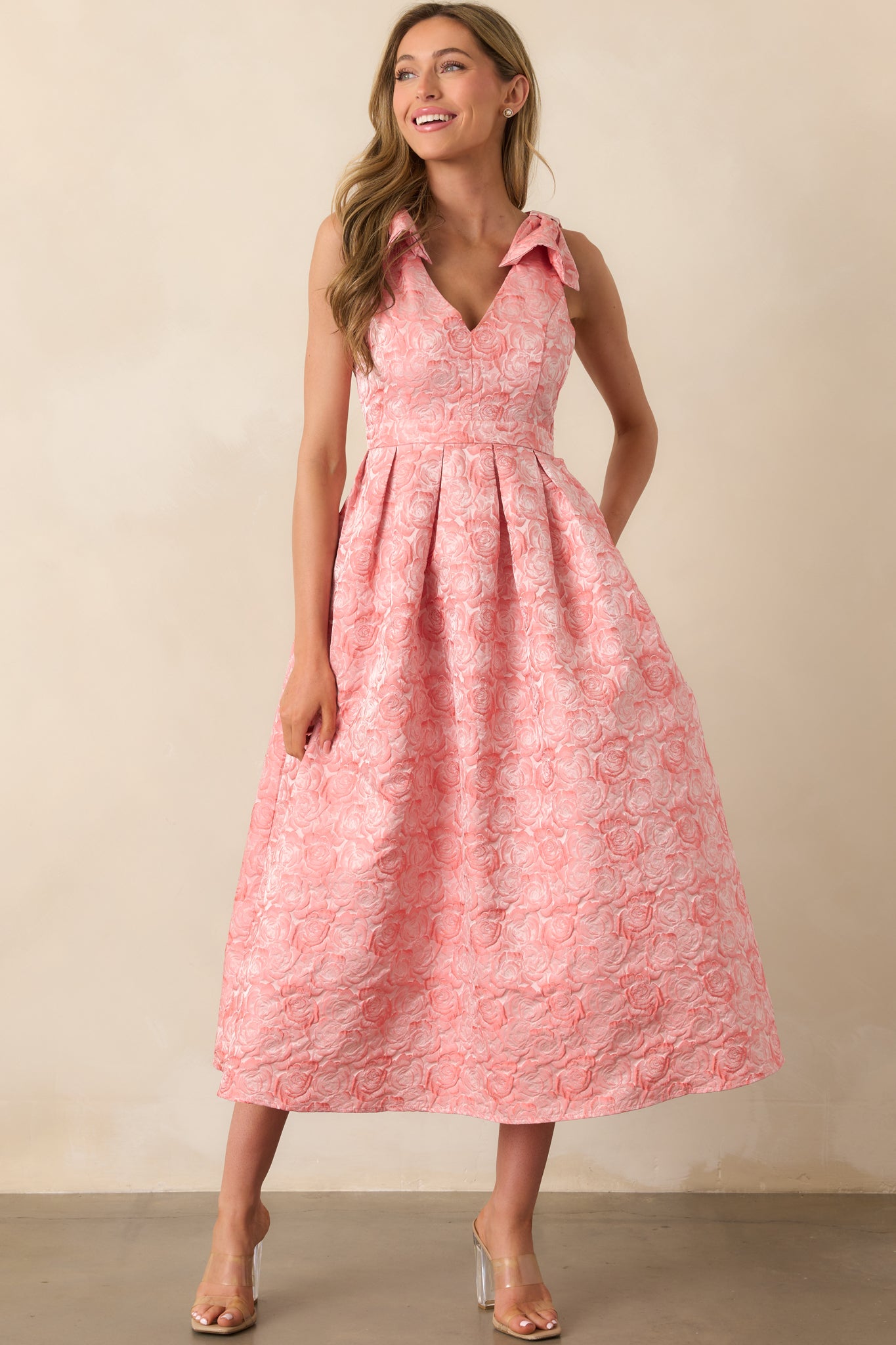 Pink coral dress with self-tie bow straps, a v-neckline, and a softly flared silhouette.