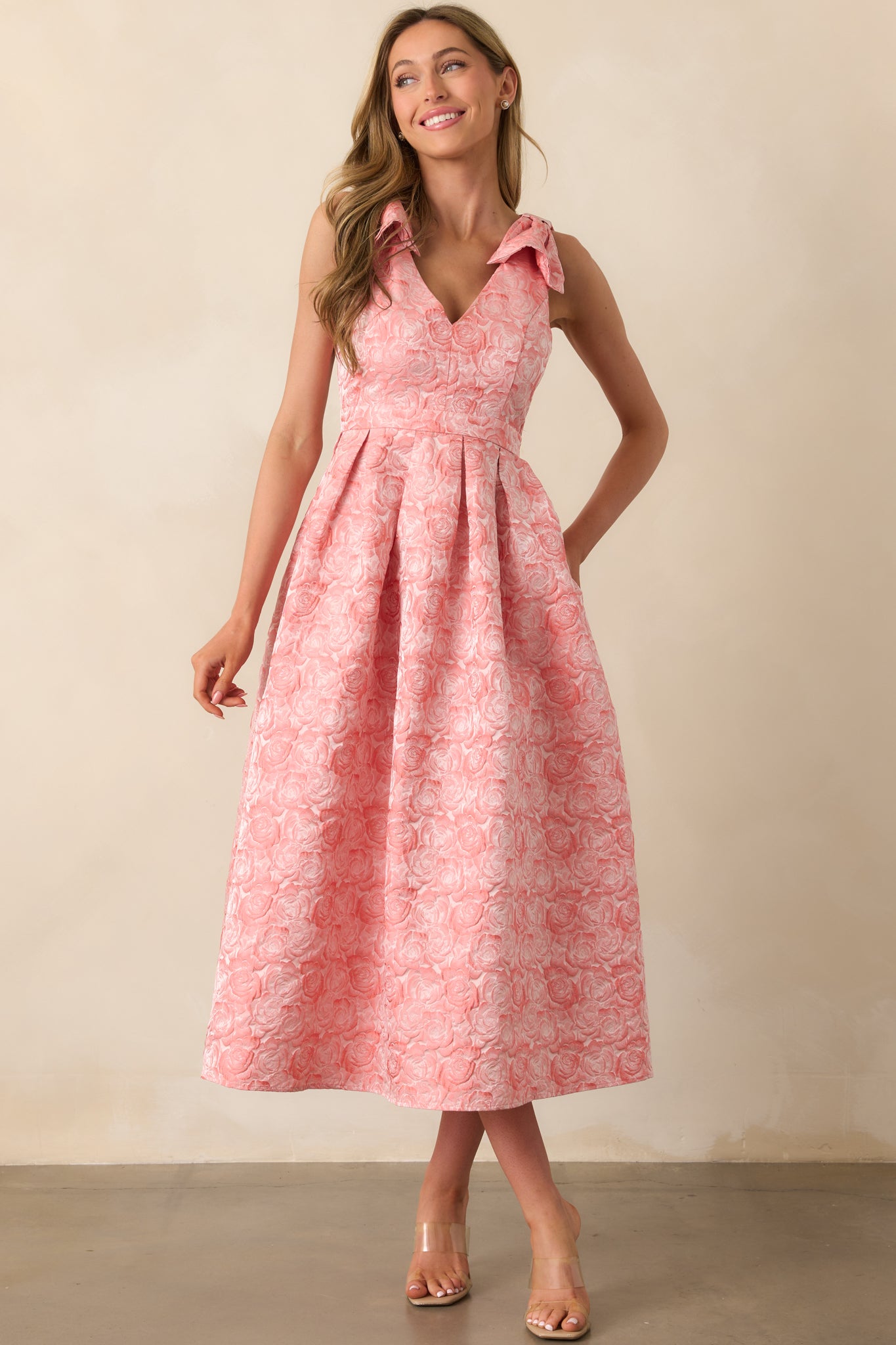 Sleeveless dress in pink coral featuring a structured bodice, bow-tied shoulder straps, and functional side pockets.