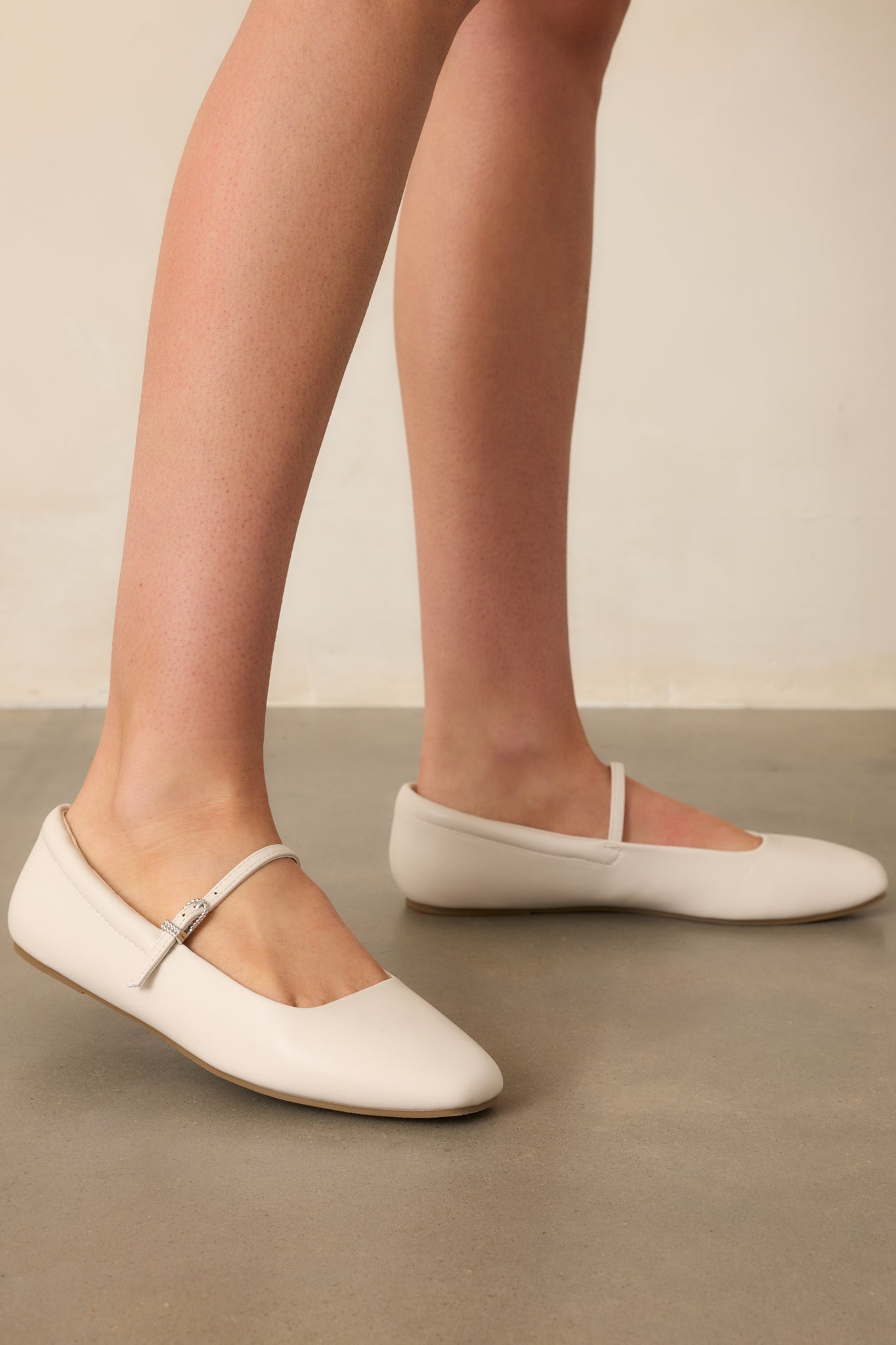 A full profile view of the flats, showcasing their ivory hue, silver buckle, and rounded toe.