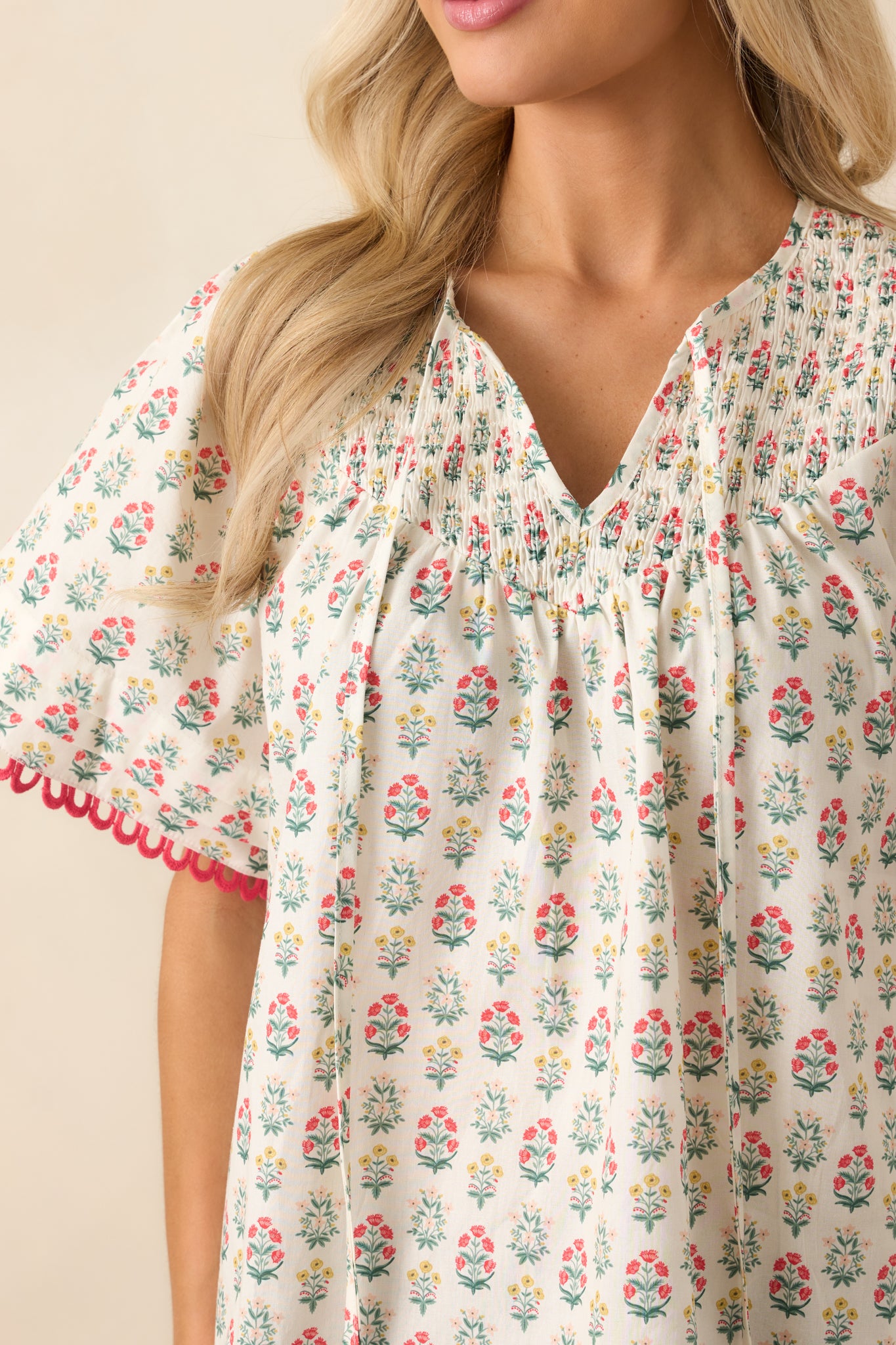 An extreme close-up capturing the texture of the smocking, embroidered trim, and fine stitching of the red floral printed top.