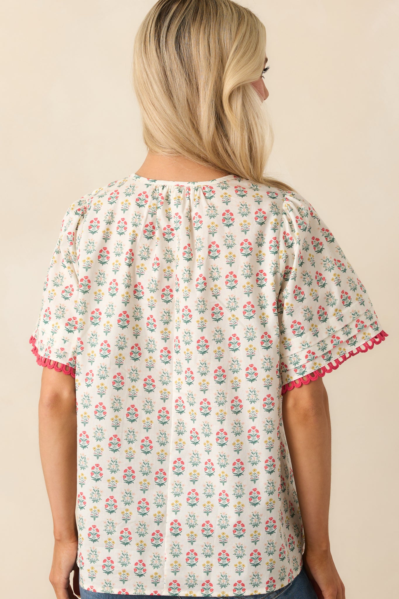 A complete back view of the top displaying the continuous red multicolor floral print and flowy back design with smocked detailing at the neckline.