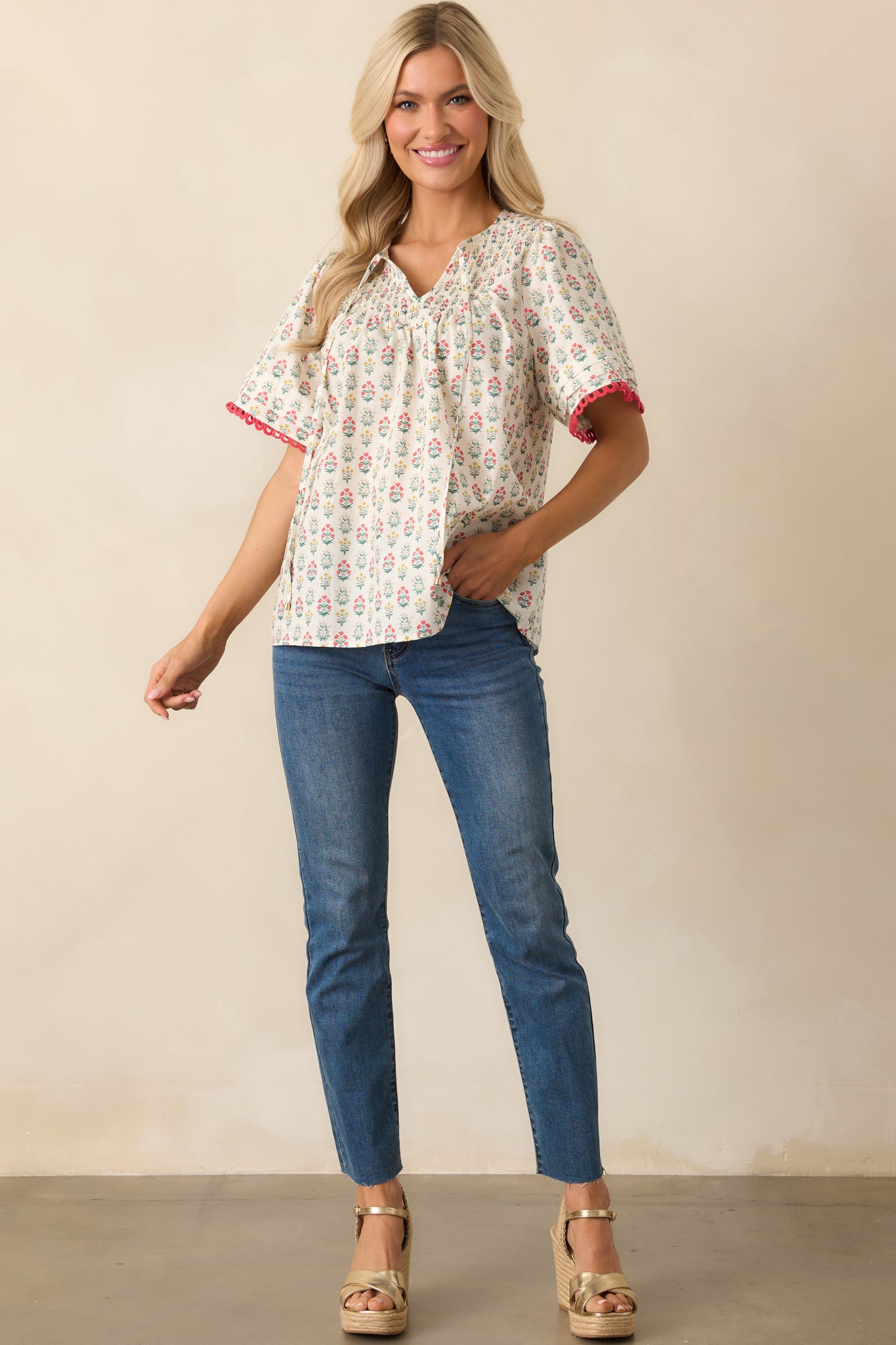 A front view of the top with red multicolor floral print, featuring a smocked yoke, short sleeves, and embroidered scallop hems.