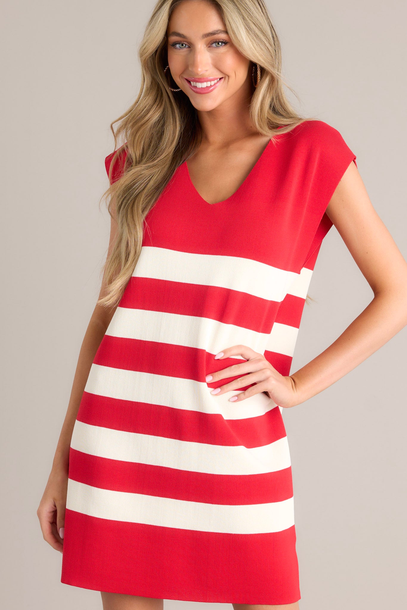 Angled view of red stripe mini dress that features a v-neckline, cap sleeves, a classic stripe pattern, a knit fabric, and a mini length. 