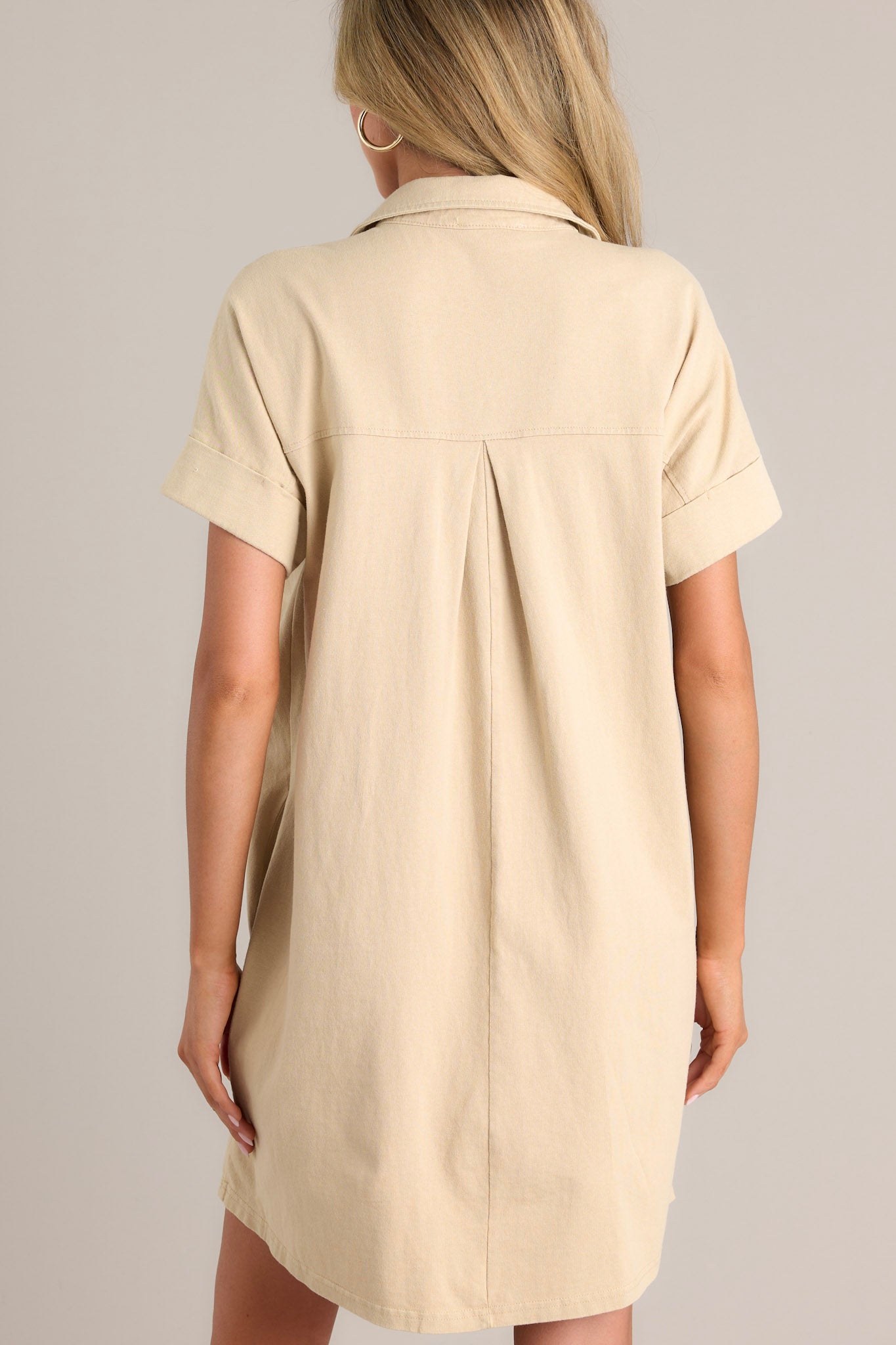 Back view of this tan mini dress that features a collared neckline, functional breast & hip pockets, and cuffed short sleeves.