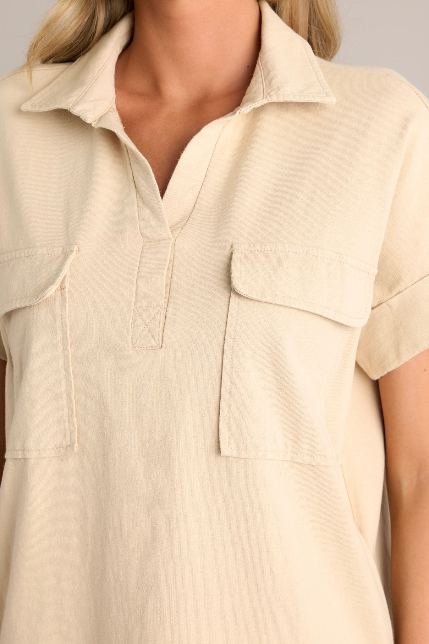 Close up view of this tan mini dress that features a collared neckline, functional breast & hip pockets, and cuffed short sleeves.
