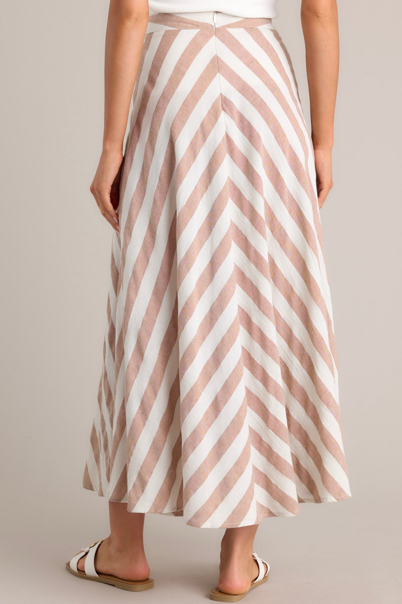 Back view of this skirt that features a high waisted design, a functional zipper and hook closure in the back, a diagonal striped pattern, and a flowy fabric.