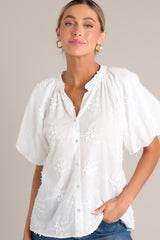 Front view of this White top with v-neckline, button front, embroidered detailing, and elastic cuffed puff sleeves.
