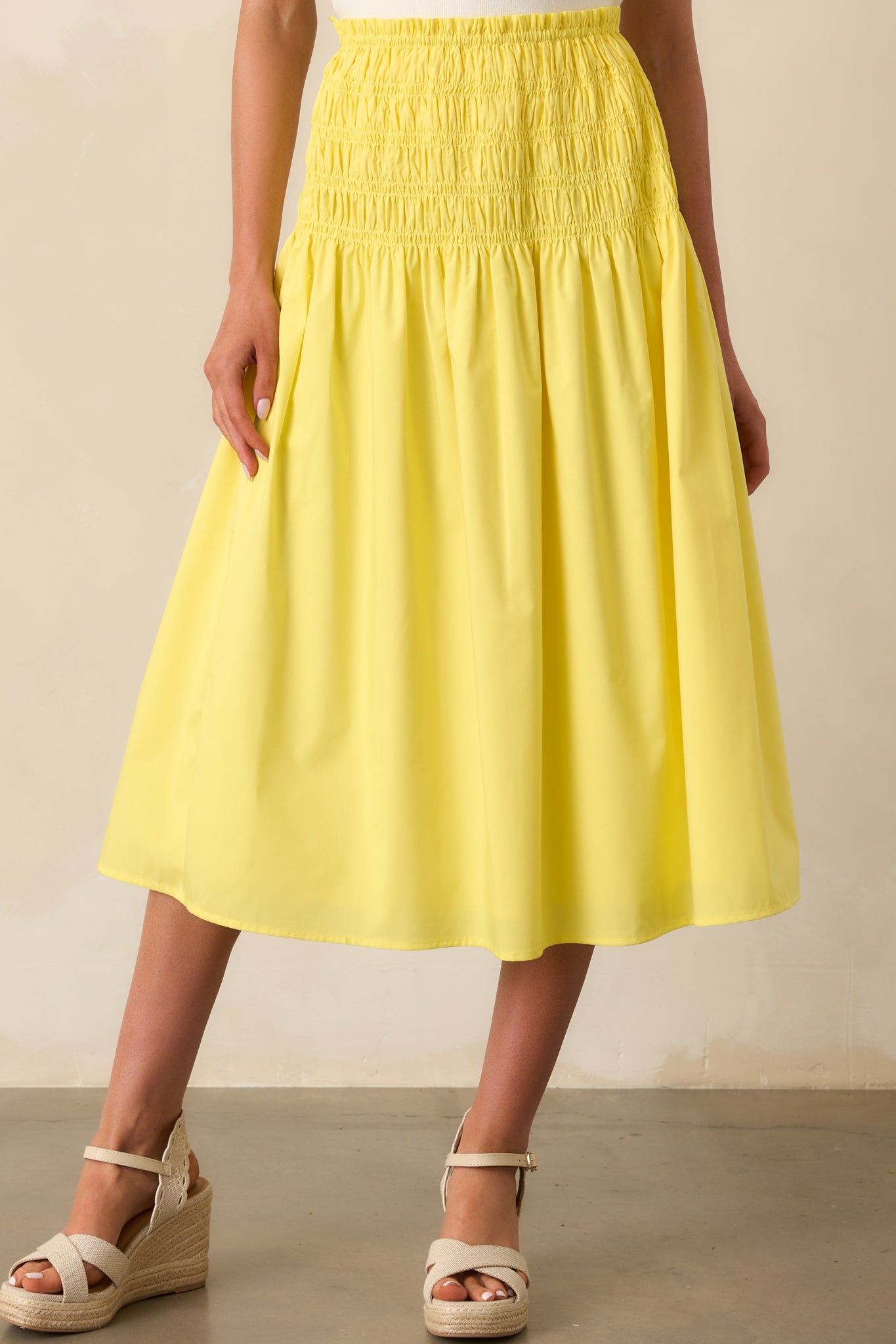 A close-up of the smocked drop waistband on the yellow skirt, showing gathered texture and a high-rise fit.