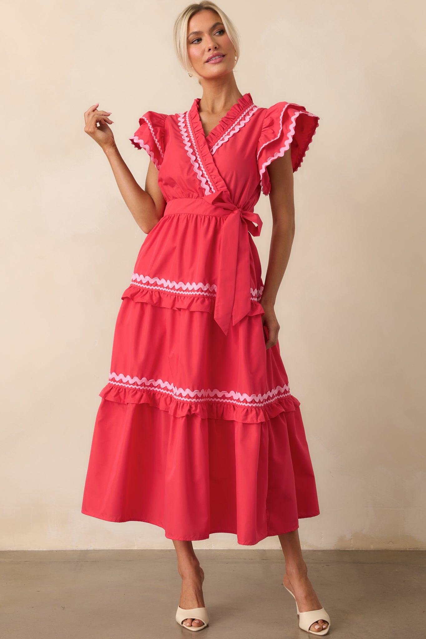 Red dress with a flowy silhouette, highlighted by pink ric rac detailing, a belted waist, and flutter sleeve design.