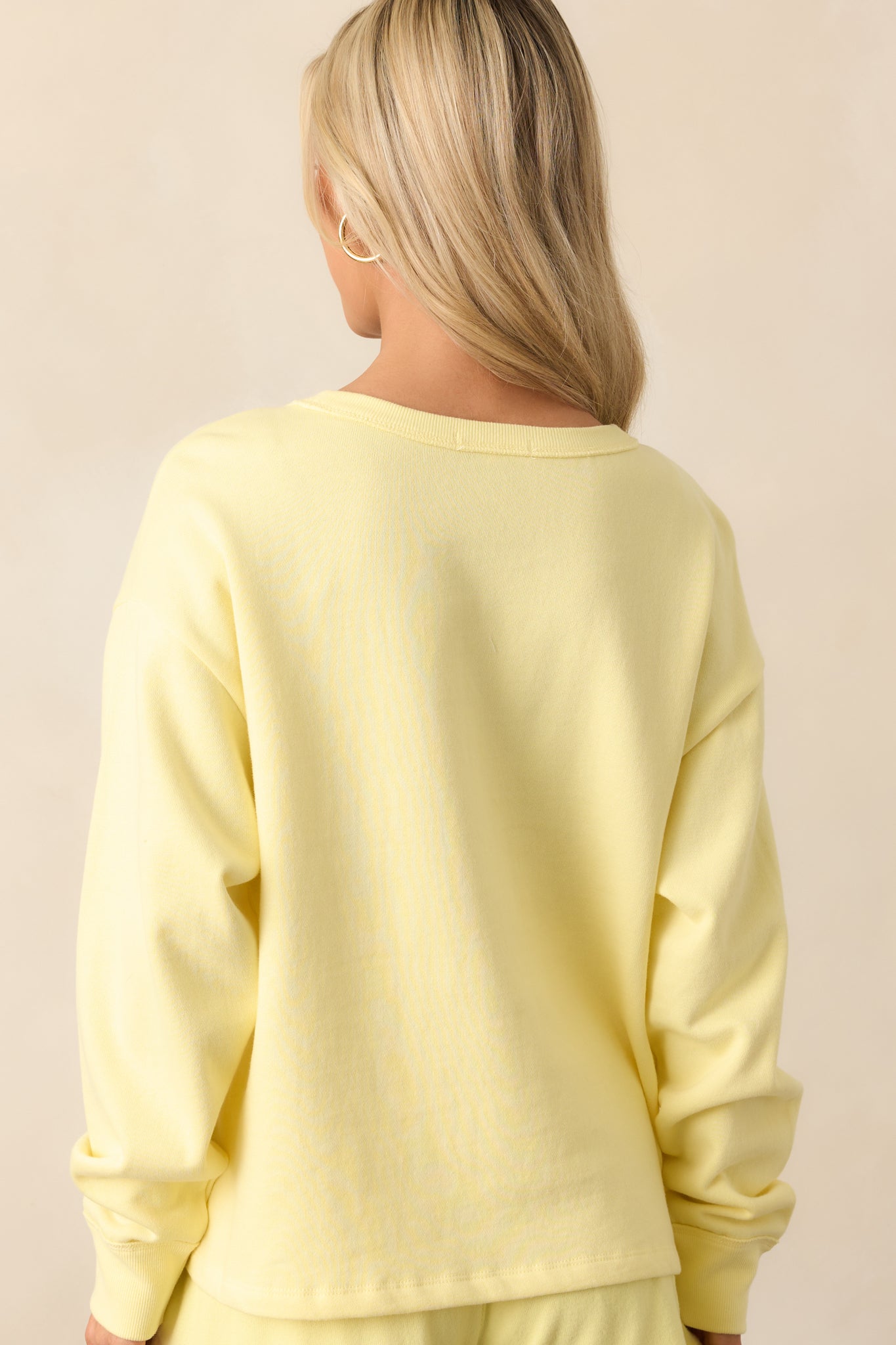 Rear view of yellow sweatshirt showing the plain back and relaxed fit silhouette with ribbed detailing.