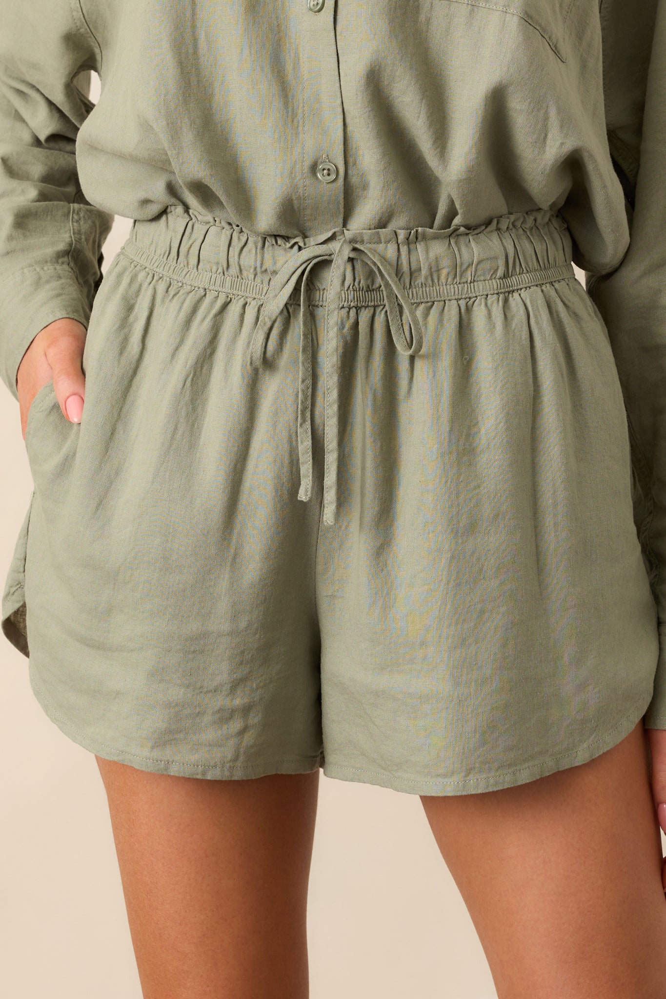 Close-up of the linen fabric texture, showcasing the stitching and drawstring design on the avocado green shorts.