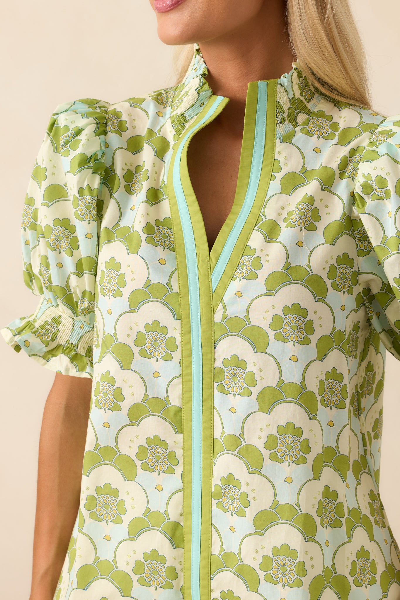 Close-up of the fabric showing the intricate smocking, ruffle trim, and floral design details on the green top.