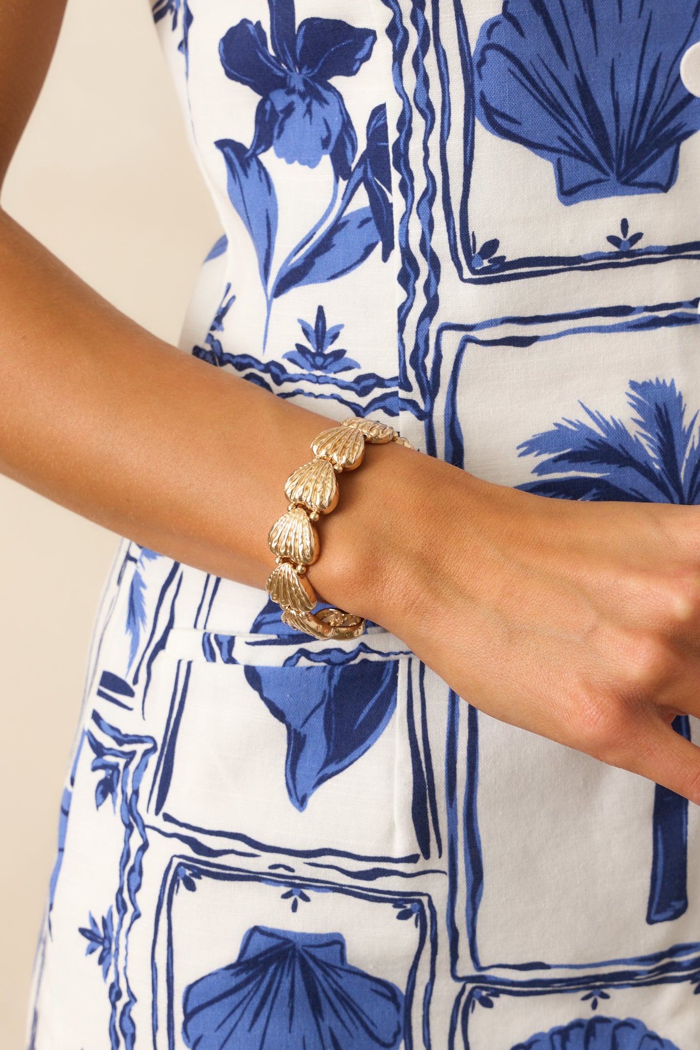 Close-up cropped shot of a bracelet with gold textured seashells placed evenly along elastic bands, allowing for an effortless slip-on design.