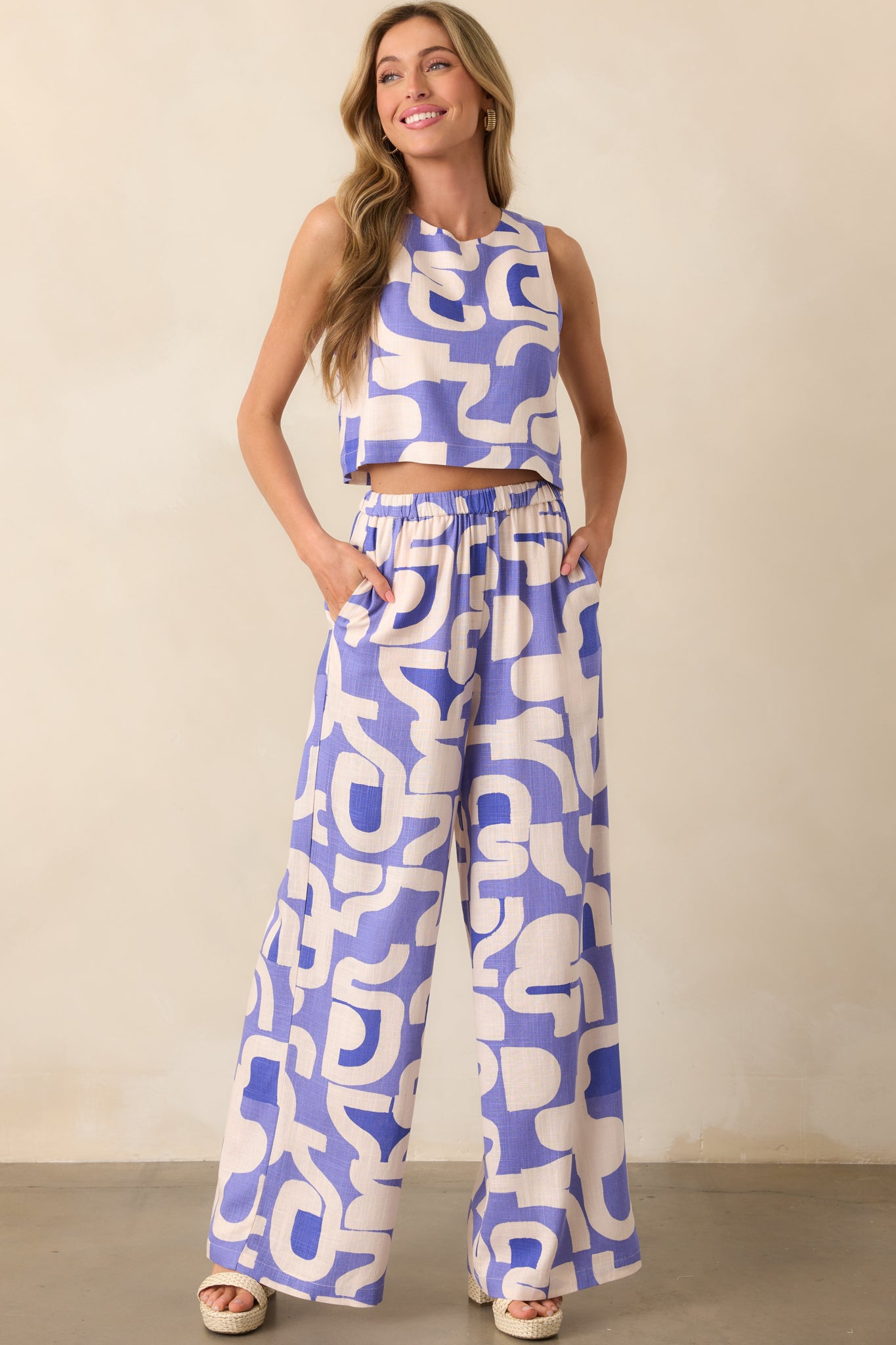 Front-facing full body view highlighting the dusty blue sleeveless top’s cropped length, relaxed boxy shape, and vibrant multicolor geometric print.