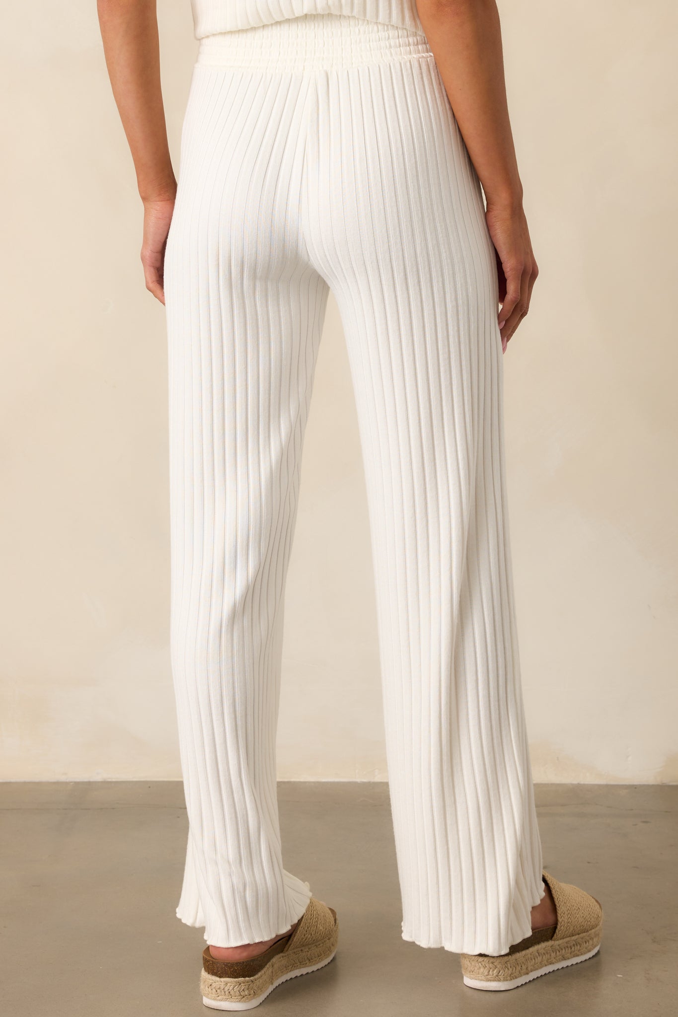 A back view of the ivory pants displaying the gathered waistband and smooth fall of the fabric through the legs.