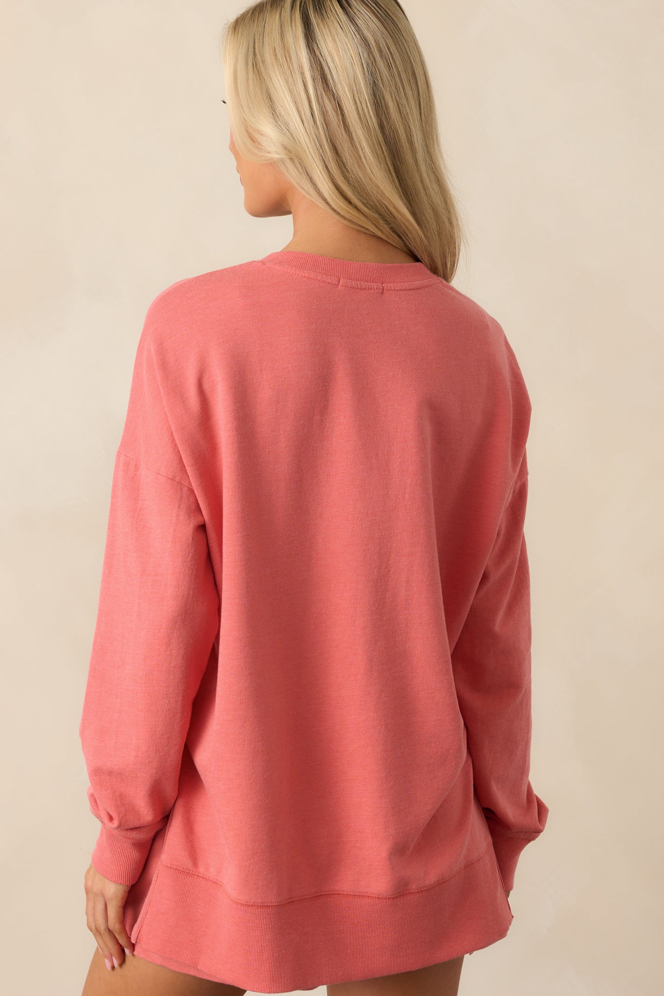 The back of this persimmon pink sweatshirt shows its oversized silhouette, with side vent slits and ribbed hems adding shape and comfort.