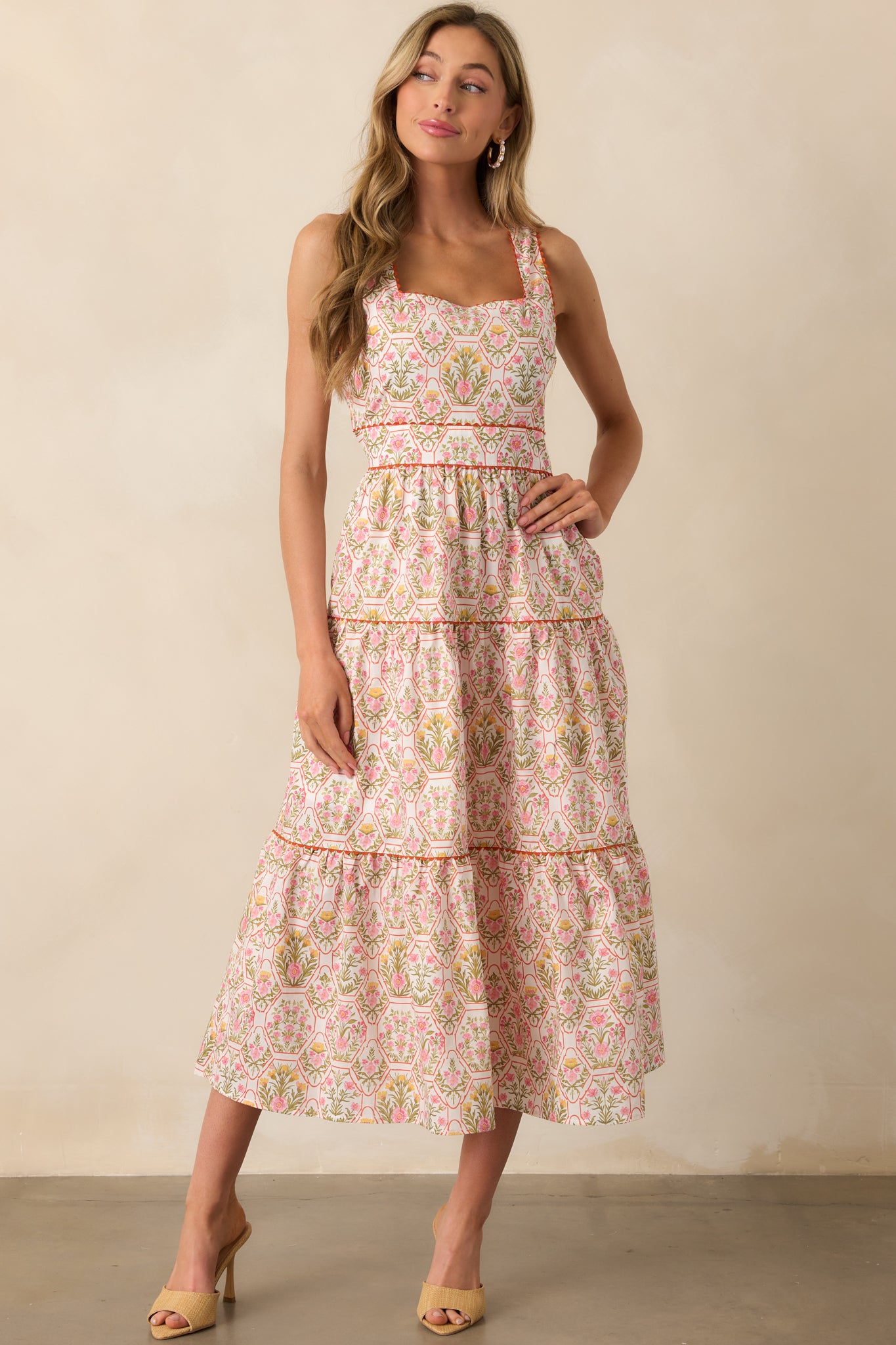 Orange printed maxi dress shown with structured square neckline, soft tiers, and floral accents throughout.