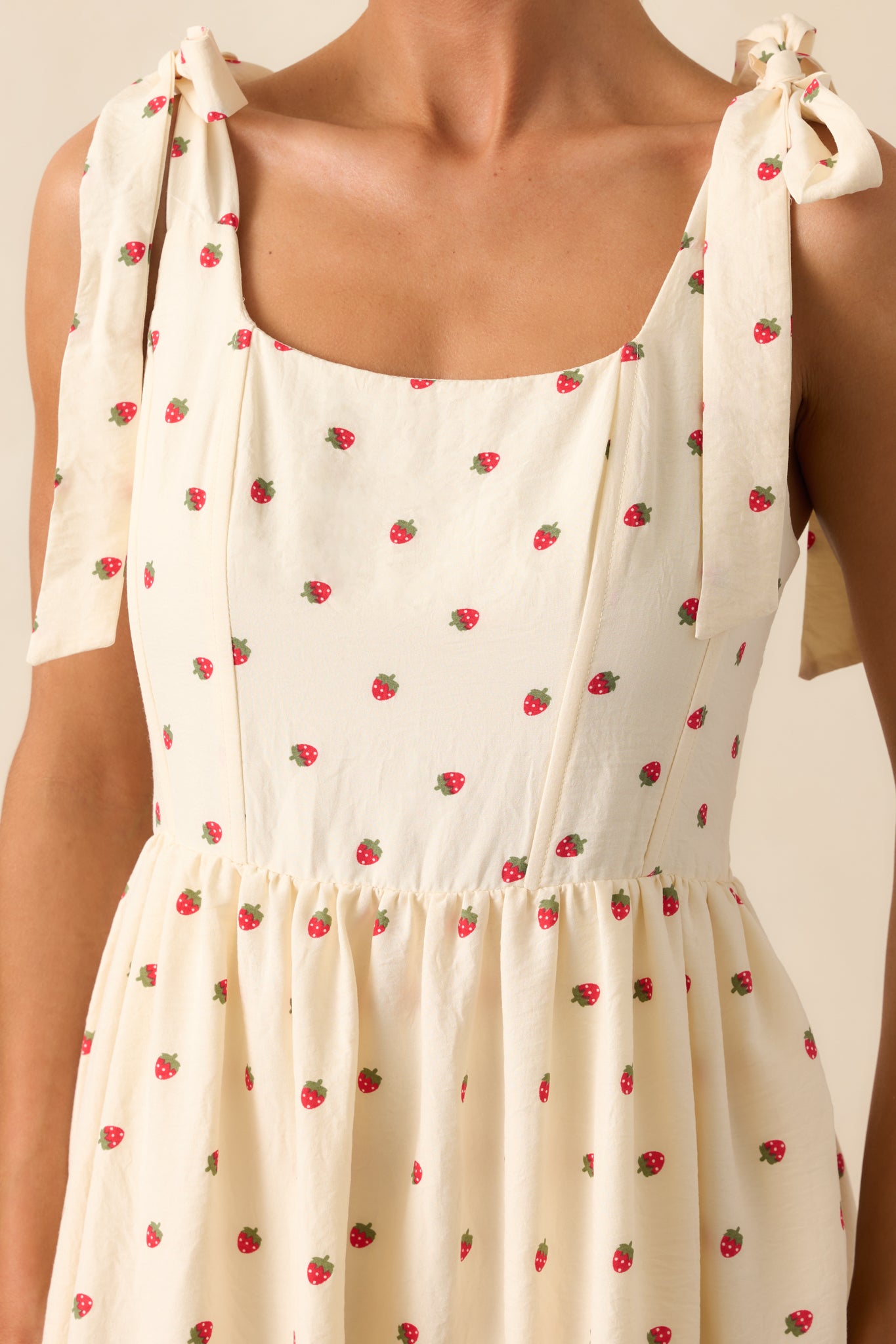 A close-up capturing the self-tie bow straps, strawberry print fabric, and detailed panel stitching at the bodice.