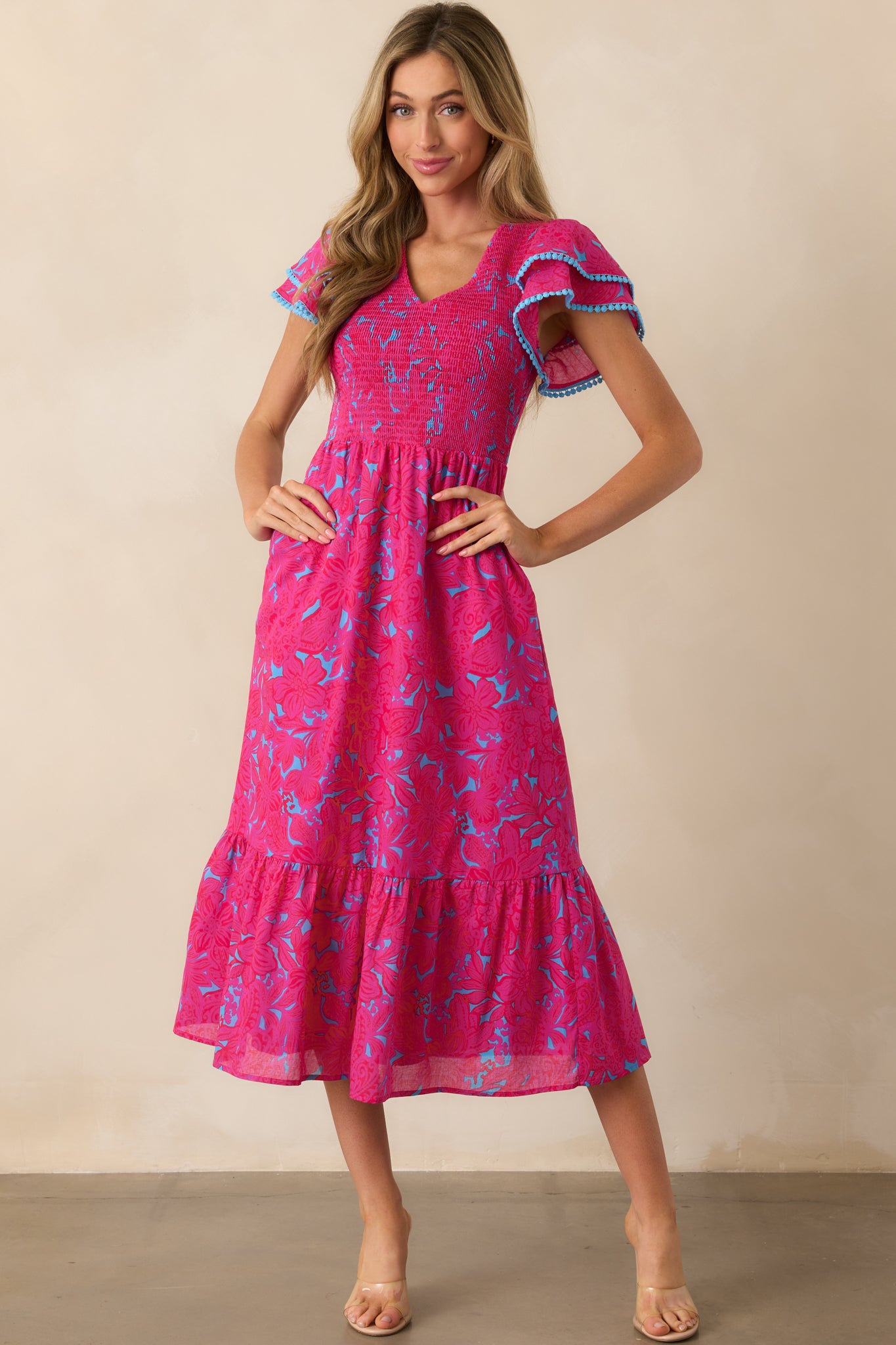 Complete front view of the fuchsia floral dress with a fully smocked bodice, v-neckline, and flowy skirt with pockets.
