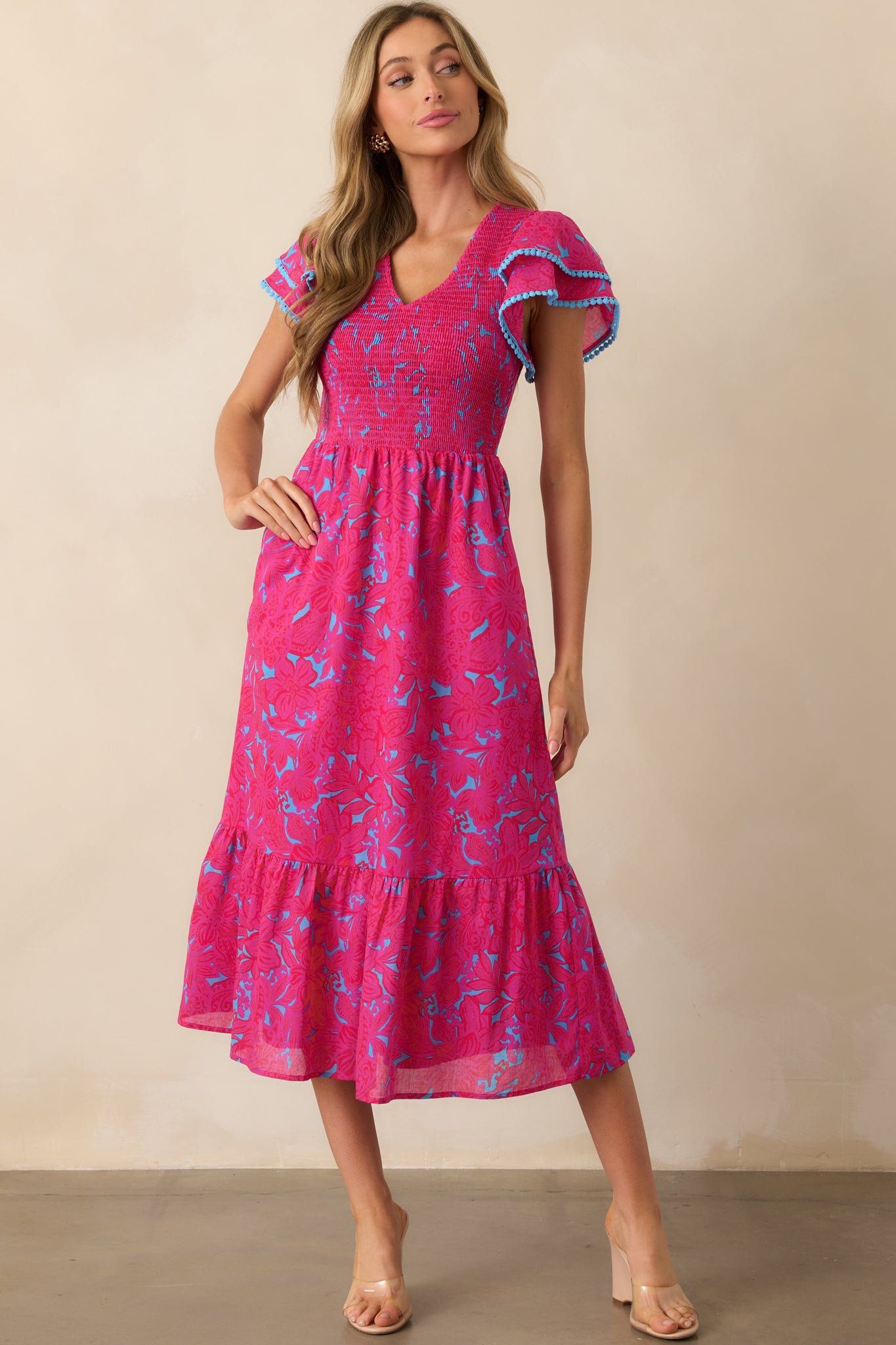 Front view of a fuchsia dress with a floral print, subtle blue background, and a v-neckline, showcasing the fully smocked bodice and flutter sleeves.