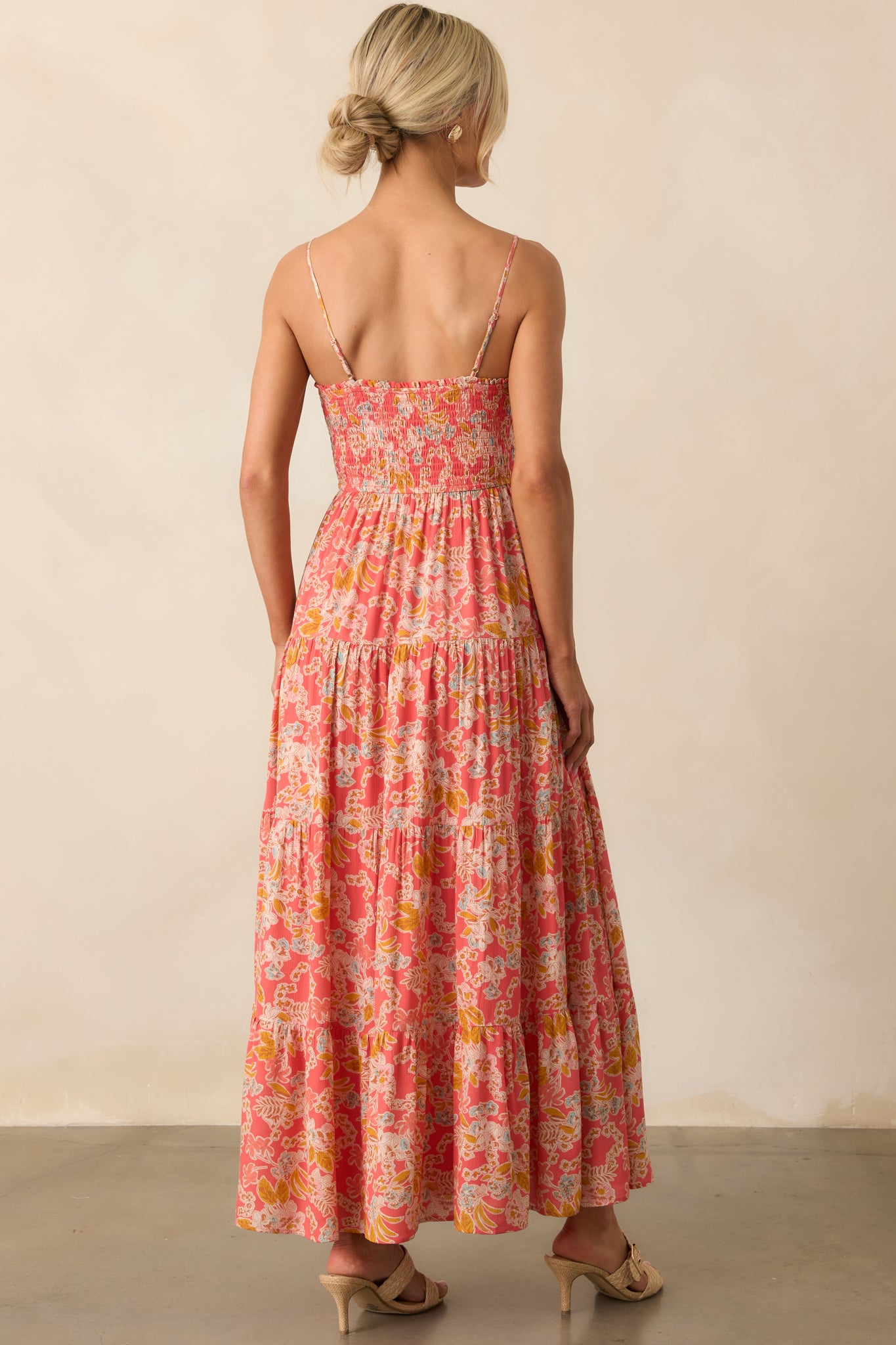 A view from behind of the pink coral dress, focusing on the back of the adjustable spaghetti straps and smooth tiered skirt.