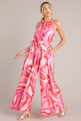  This pink multi jumpsuit features a high haltered neckline with a braided self tie detail, open back, adjustable belt, pockets at the thigh, and a wide leg.