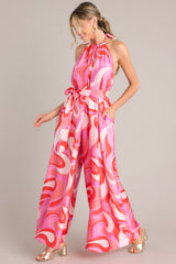 Full body view of this jumpsuit that features a high haltered neckline with a braided self tie detail, open back, adjustable belt, pockets at the thigh, and a wide leg.