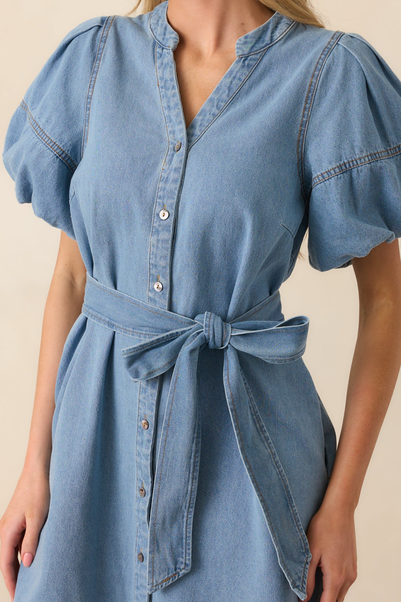 Close-up of the dress's light wash fabric, button hardware, and stitching detail around the pocket and belt loop