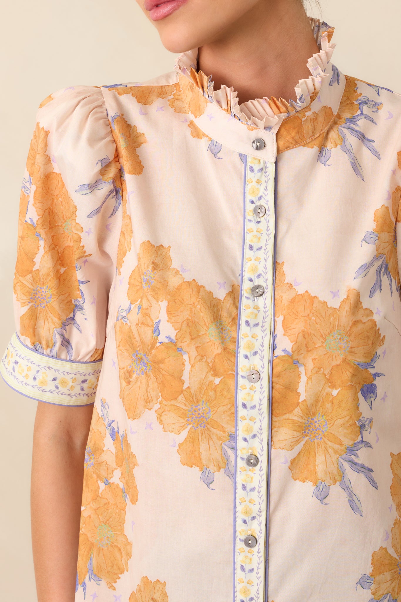 An extreme close-up capturing the mock high neckline, contrast floral trim, and fine stitching of the honey yellow top.