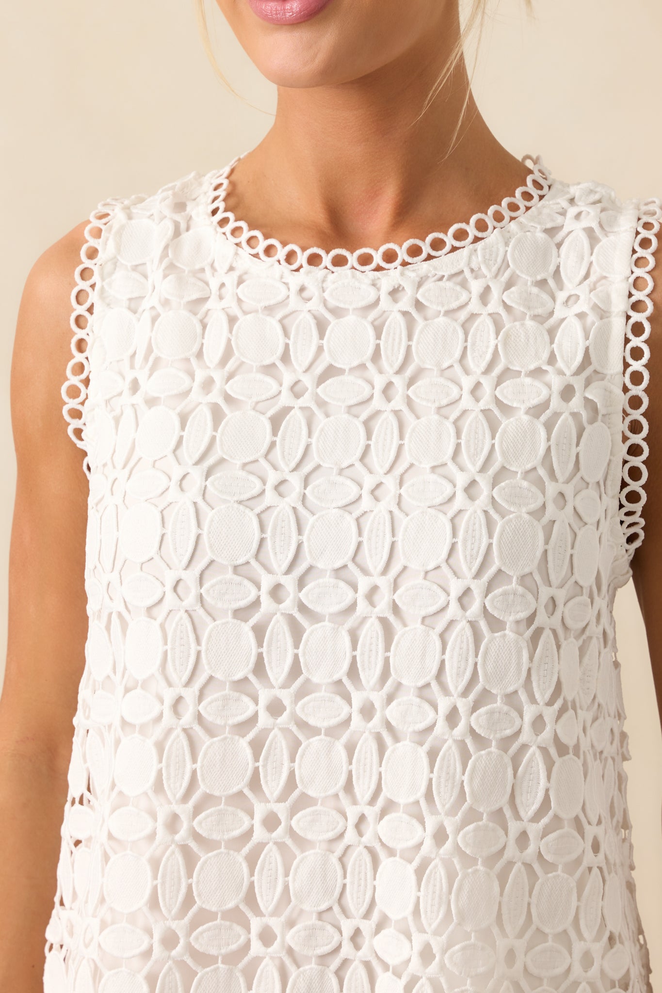 Close-up of white geometric embroidered eyelet fabric with circle eyelet trim and soft white lining visible beneath.