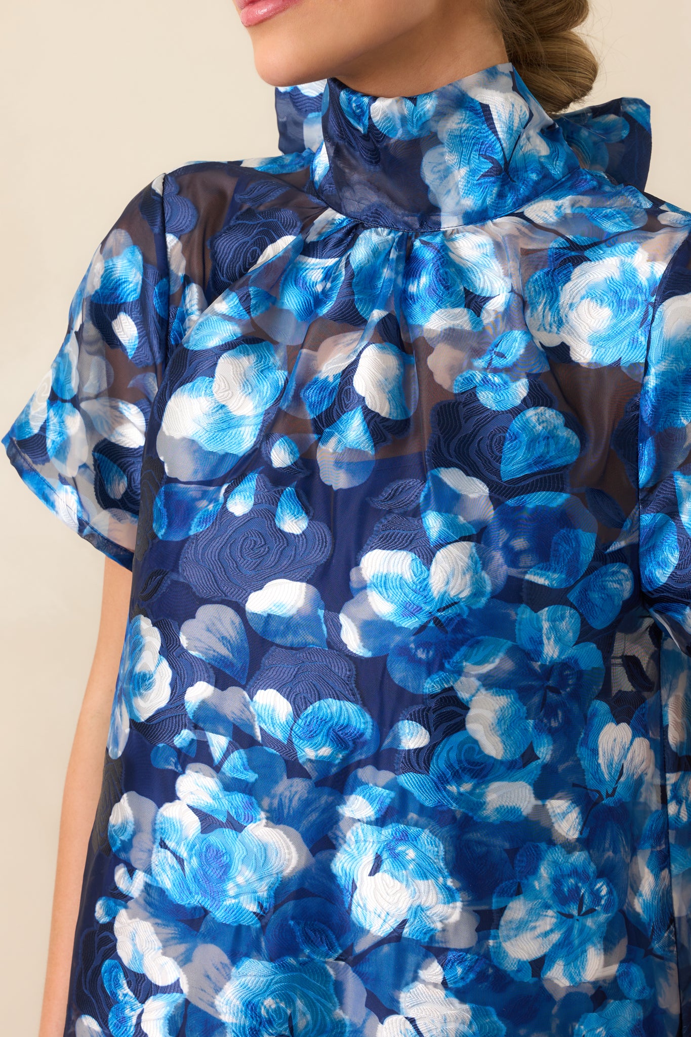 Detailed shot of the high turtle neckline, highlighting the soft structure of the collar and the delicate blue floral pattern surrounding it.