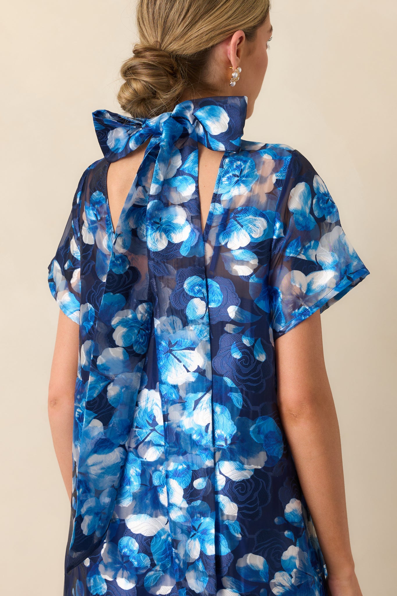 Close-up view of the dress’s self-tie bow at the neckline, showing the sheer floral fabric and part of the detachable slip beneath.