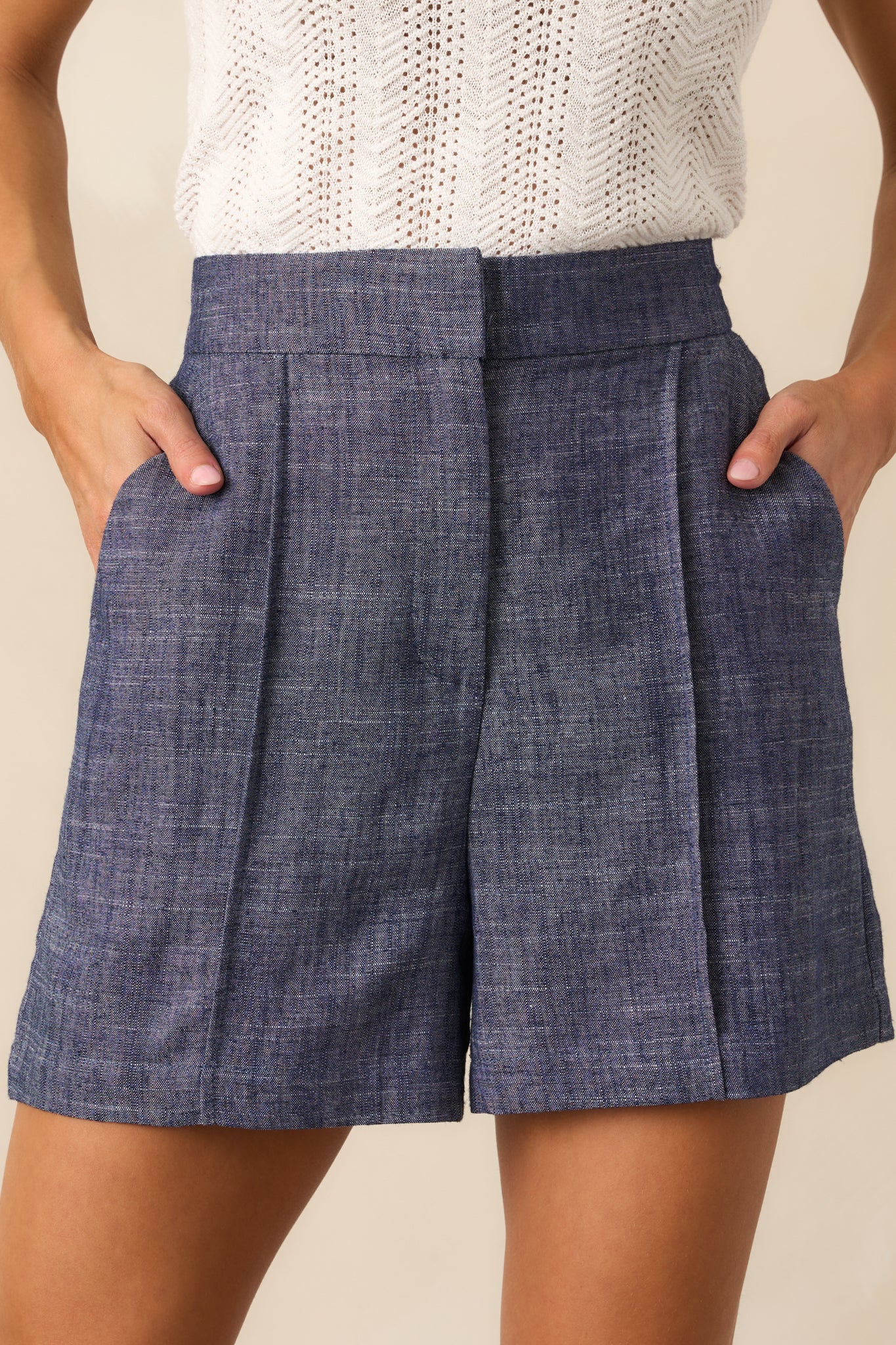 Close-up detail of tailored dark wash shorts highlighting the zipper and hook and bar closure with visible pleat stitching.