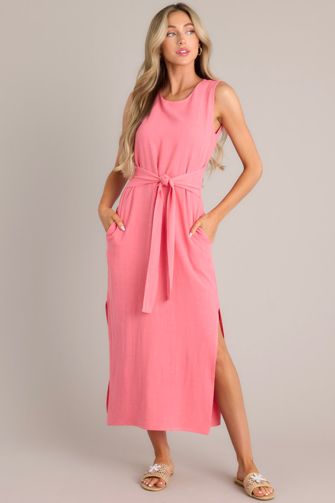 Full body view of this coral dress that features a rounded neckline, a back keyhole cutout with functional button, a smocked back insert, a self-tie waist feature, functional hip pockets, and side slits.