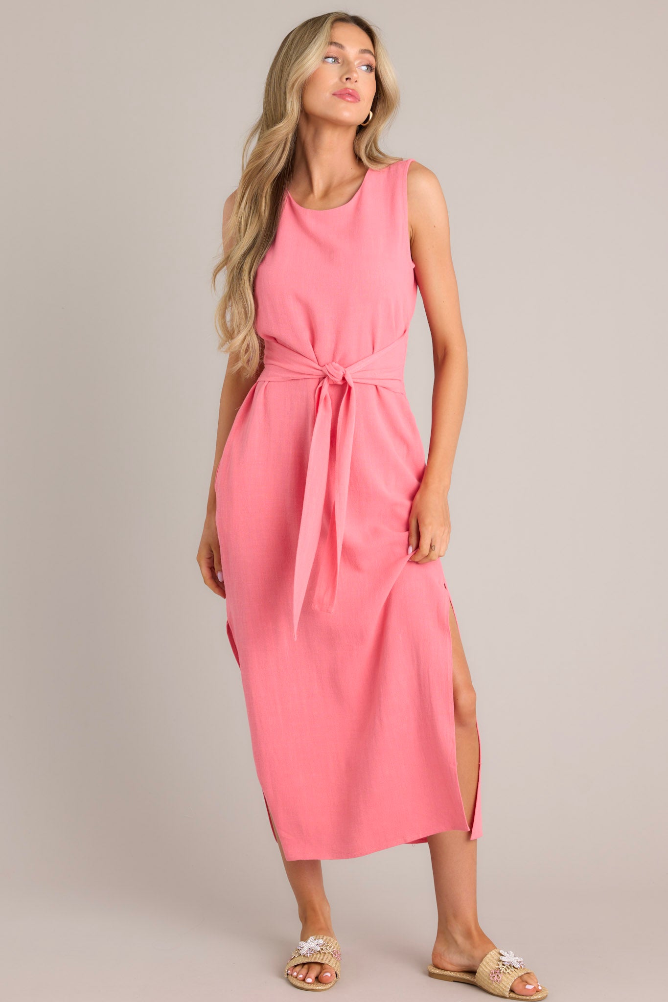 Front view of this coral dress that features a rounded neckline, a back keyhole cutout with functional button, a smocked back insert, a self-tie waist feature, functional hip pockets, and side slits.