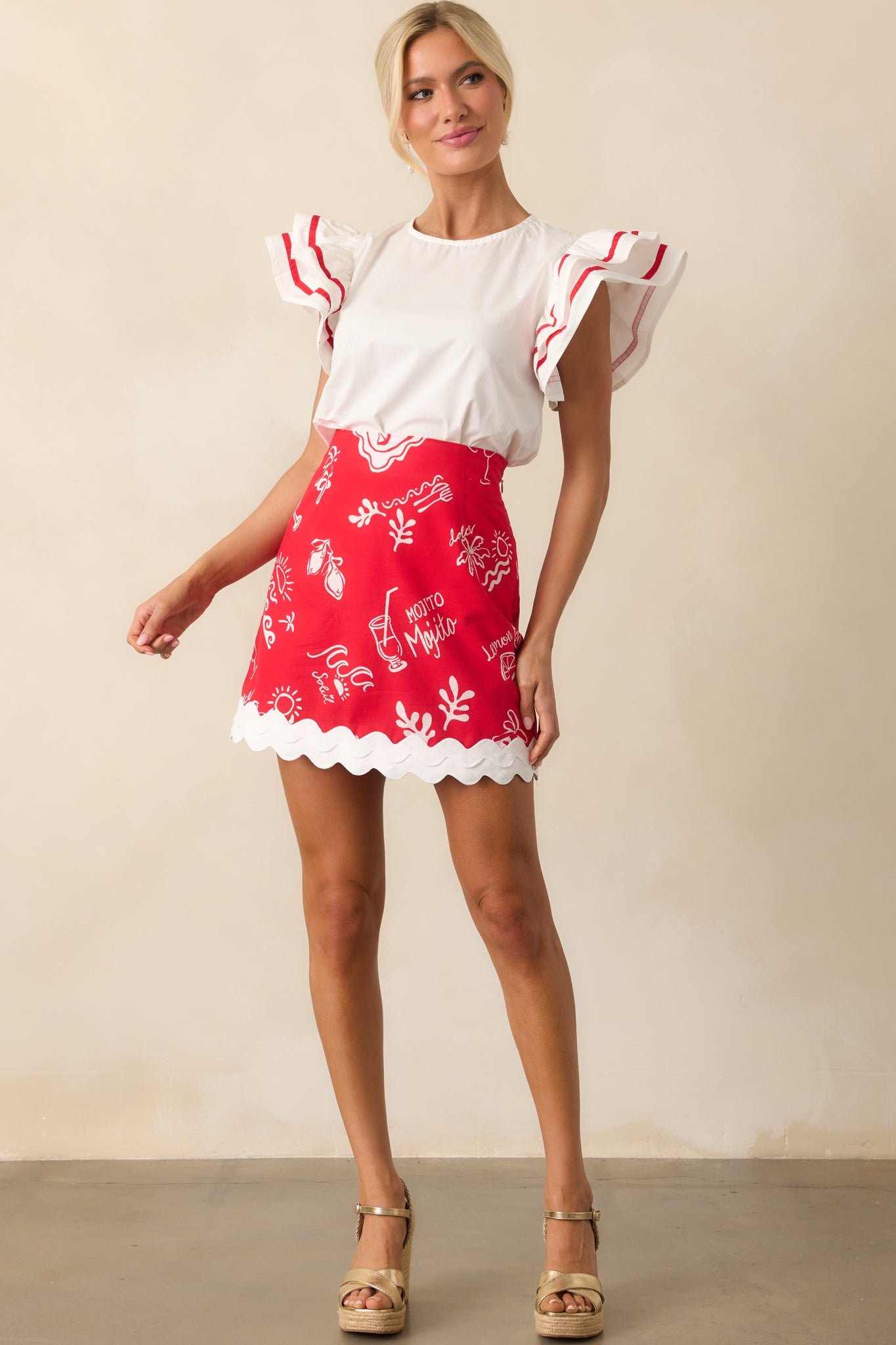 The white top with oversized flutter sleeves and red piping shown in full view, emphasizing the flowy fit and round neckline.