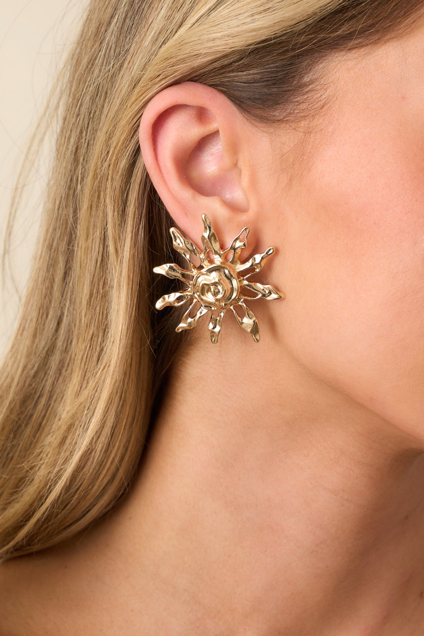 An extreme close-up capturing the textured gold finish, swirling center motif, and post backing of the sun-shaped earrings.