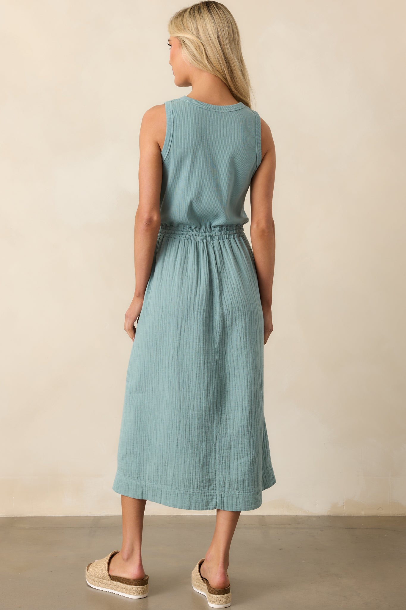 A view from behind of the sage midi dress, showing the ribbed upper section and gentle drape of the skirt.