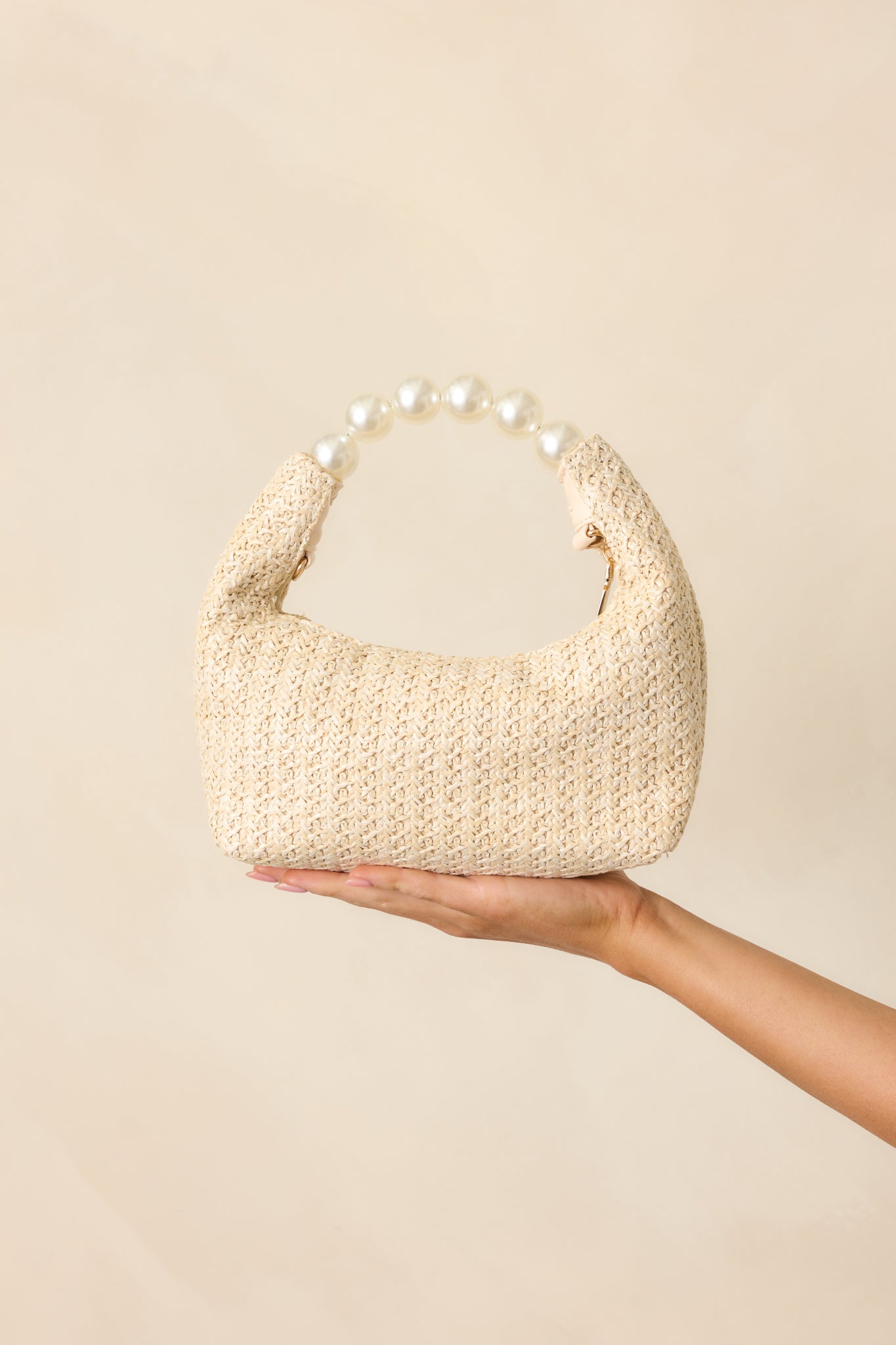 A front view of the ivory rattan handbag with a structured faux pearl handle and gold zipper closure.