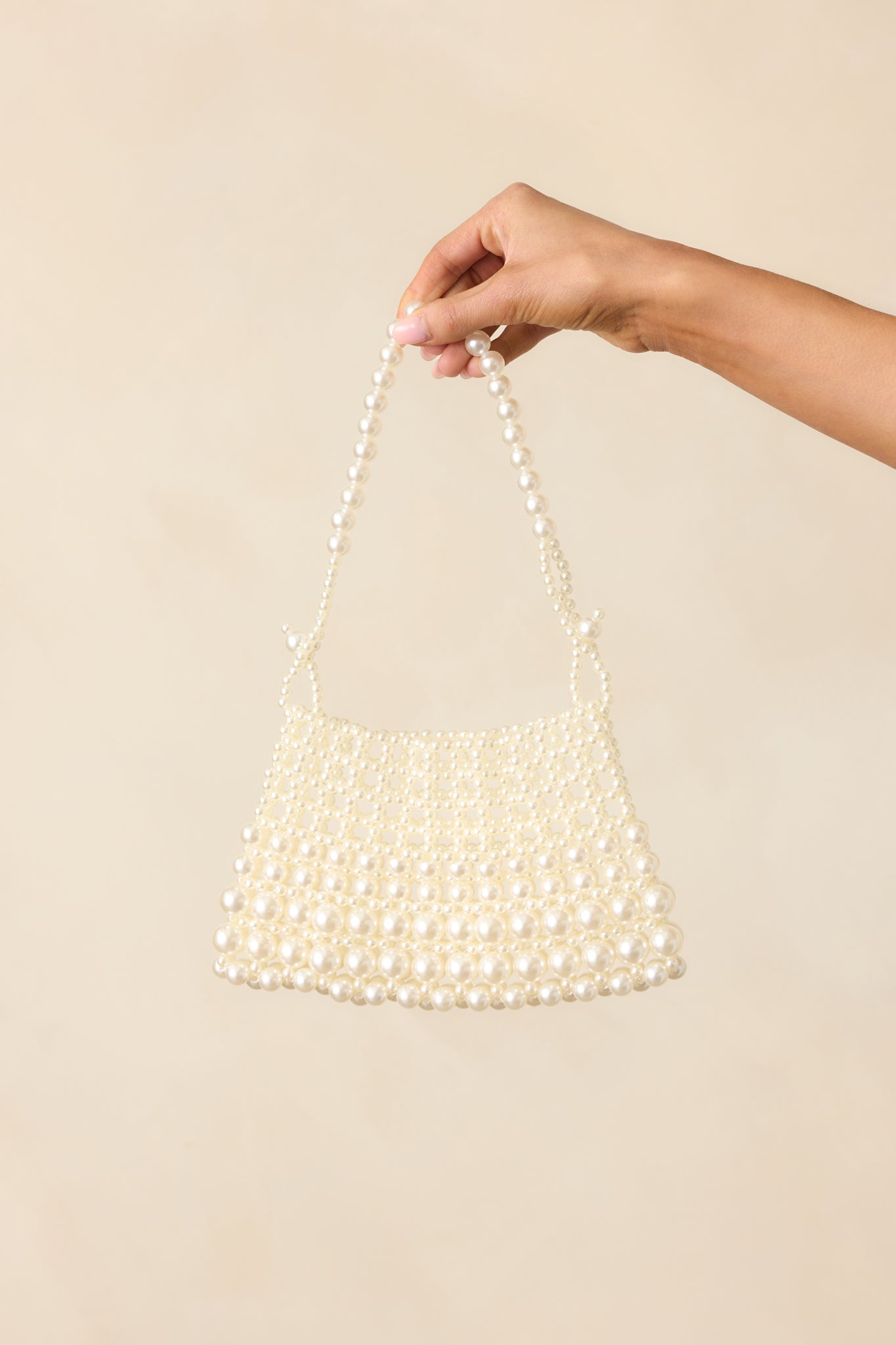 Close view of the handbag’s top-handle with visible knot detailing and clustered ivory faux pearls.