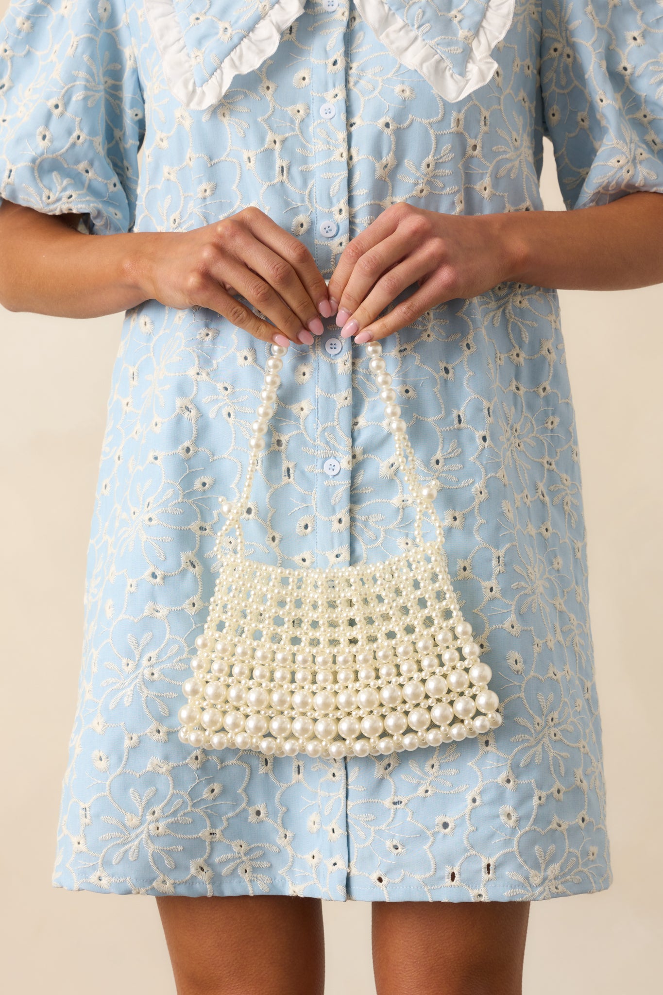 Ivory beaded handbag with a structured silhouette and knotted top-handle, featuring various sized faux pearls throughout.