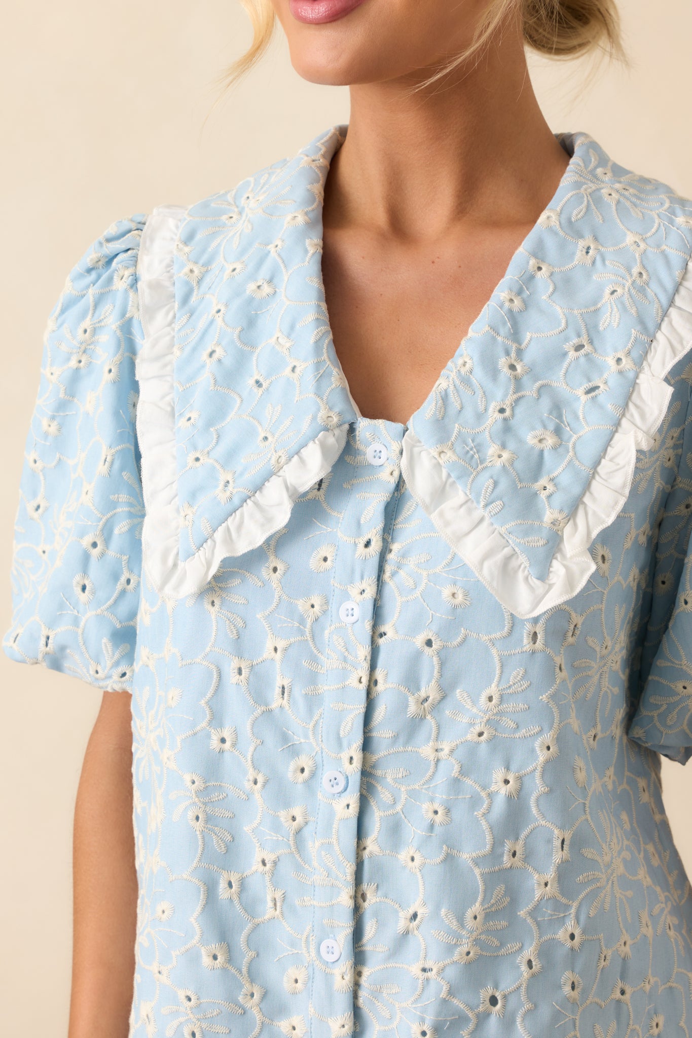 Close-up of embroidered eyelet fabric with ruffle trim along the collar and fine stitching.