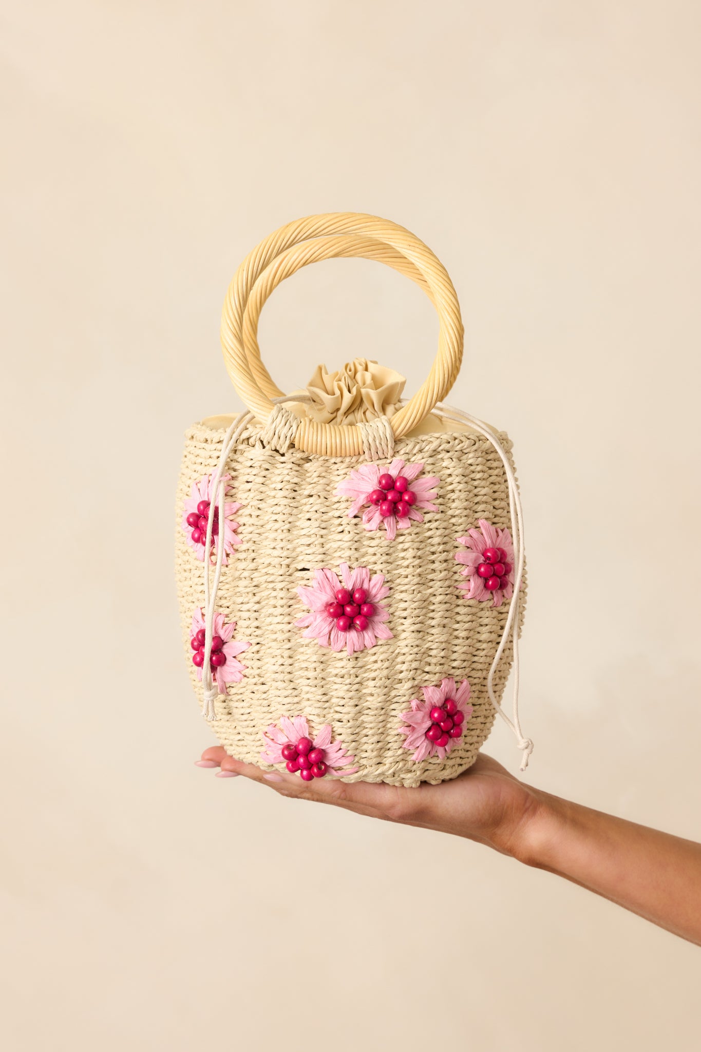 A partial view of the handbag, focusing on the woven straw texture and delicate pink straw flowers.